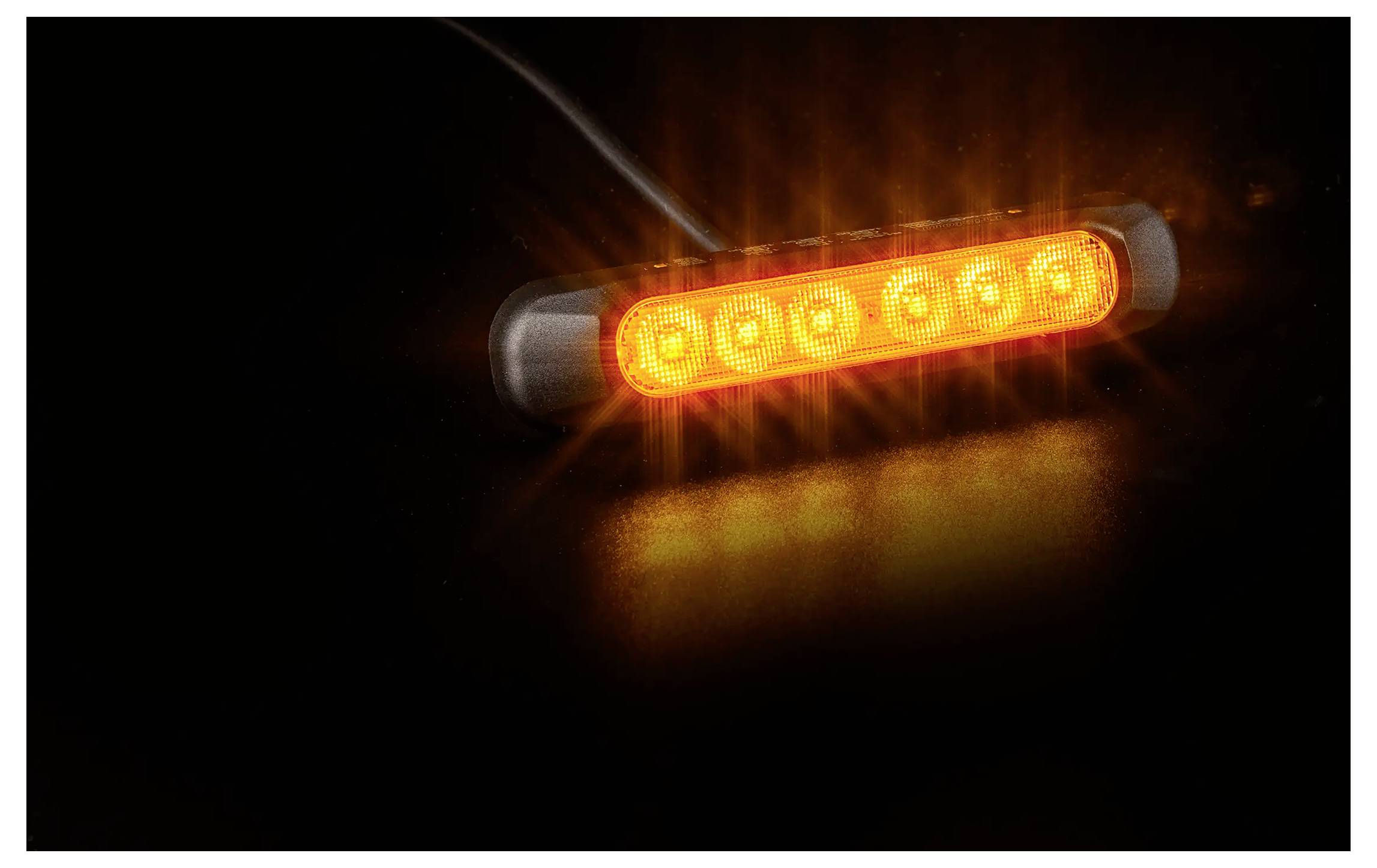 Oranžové LED varovné světlo svítící v tmě na černém pozadí, zobrazeno v detailním záběru.