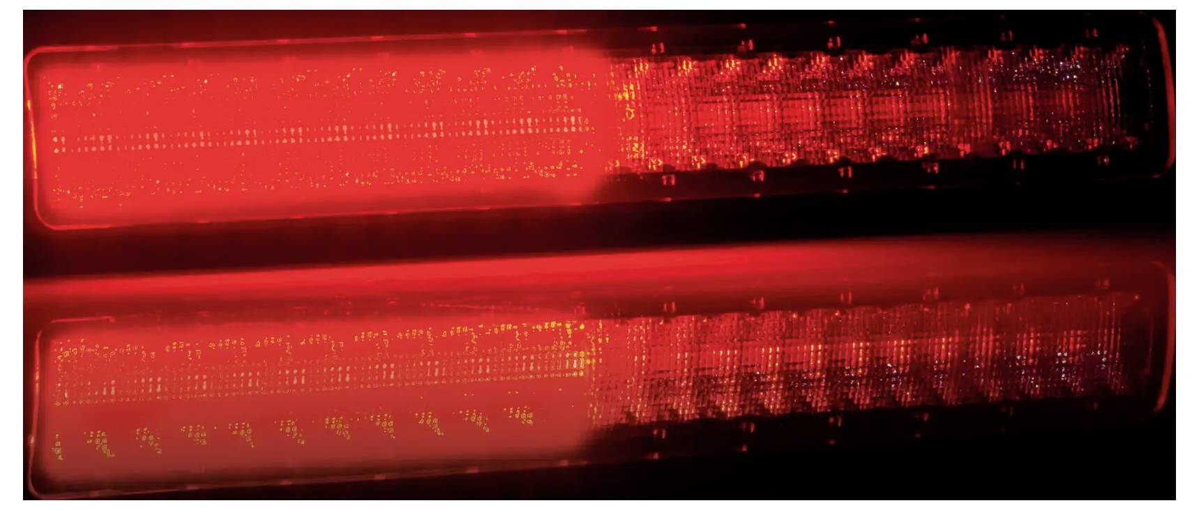 Detailní snímek dvou svítících červených LED světelných lišt na tmavém pozadí, pravděpodobně brzdových nebo signalizačních světel.