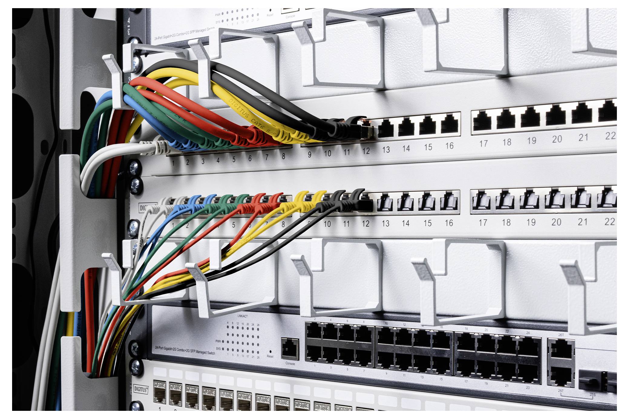 Detailní záběr na síťový přepínač a patch panel s barevně označenými kabely Ethernet připojenými v serverovém racku.