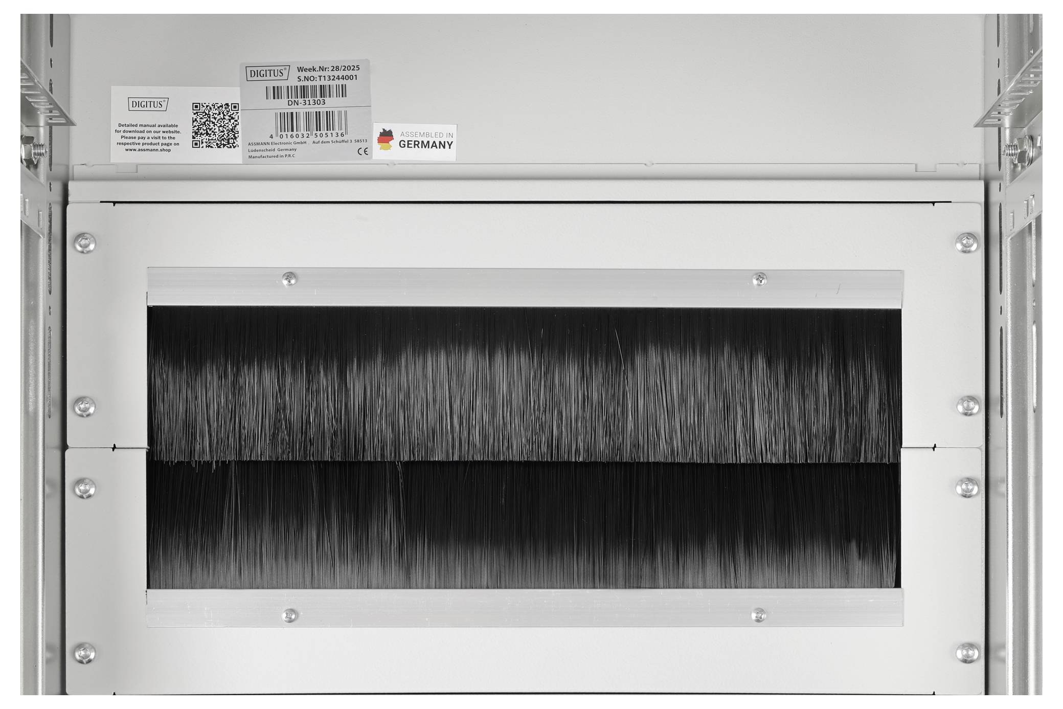 Detailní pohled na kovovou ventilační jednotku s úzkým otvorem zobrazující husté černé štětiny nebo vlákna uvnitř, namontované v regálu.