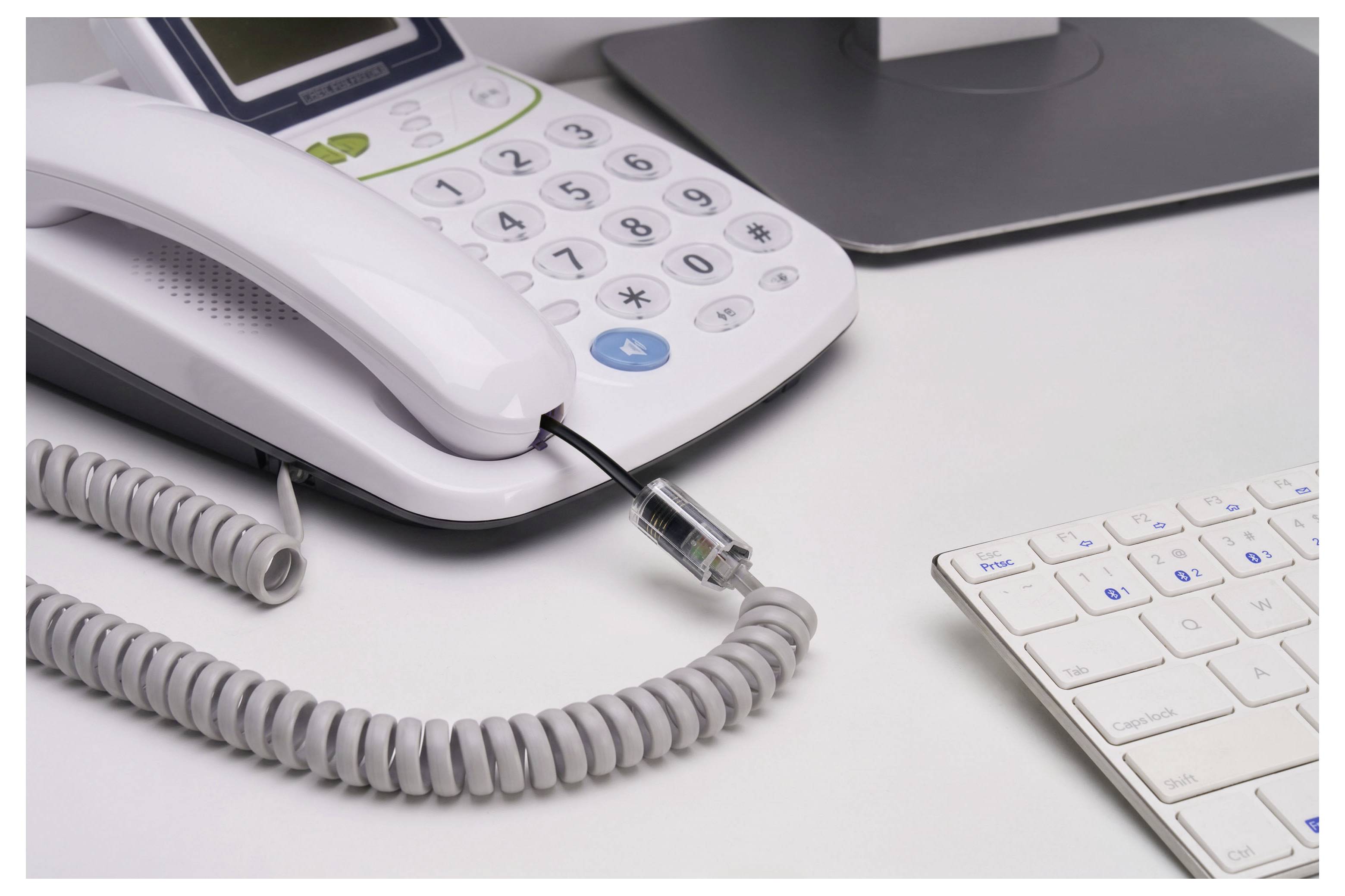 Bílý kancelářský stůl s desktopovým telefonem, spirálovým kabelem, ethernetovým kabelem, notebookem a klávesnicí, což naznačuje kabeláž v kancelářním pracovním prostoru.