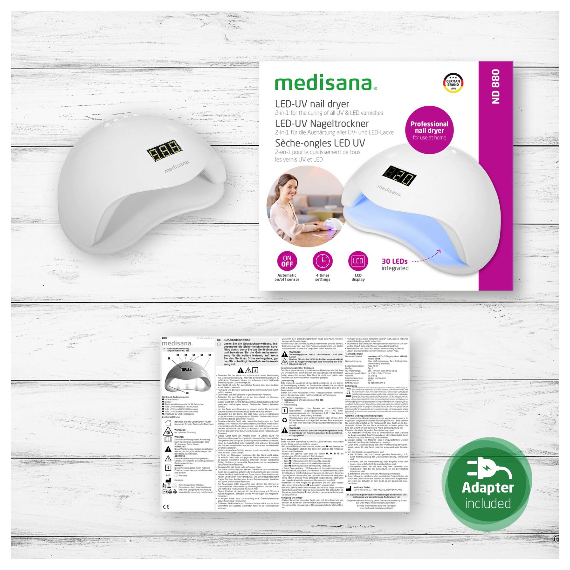Medisana LED-UV vysoušeč nehtů zobrazený s krabicí produktu, návvodem k použití a zeleným odznakem "Adaptér je součástí balení" na bílém dřevěném pozadí.