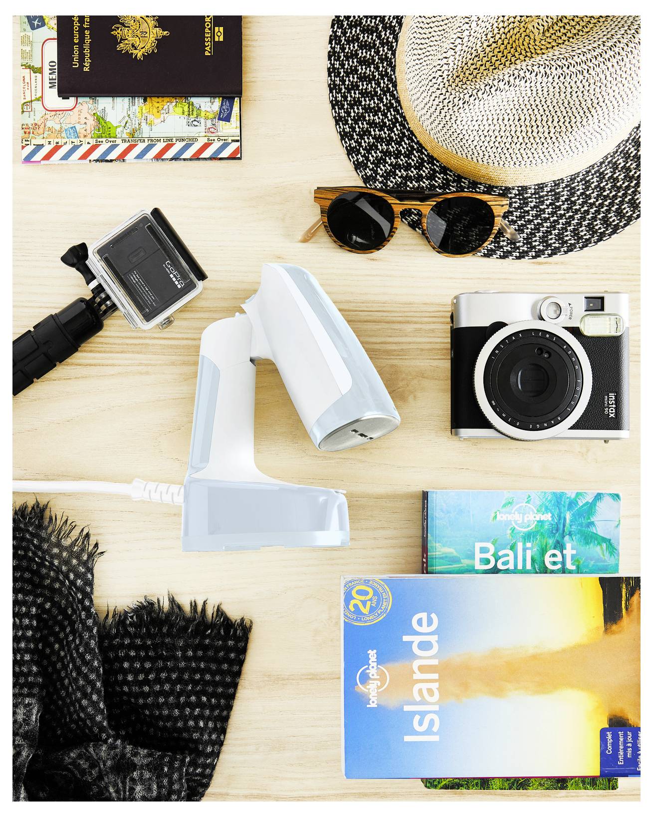 Cestovní arrangement s fotoaparátem, GoPro, pasem, slunečními brýlemi, letním kloboukem a průvodci pro Bali a Island na dřevěném povrchu.