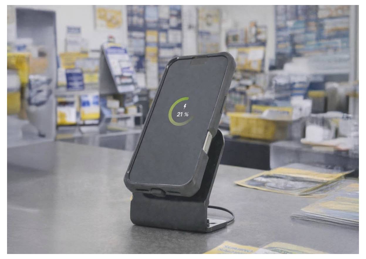Smartphone na nabíjecím stojanu zobrazující 21% baterie v oblasti maloobchodního pokladny nebo servisního pultu.
