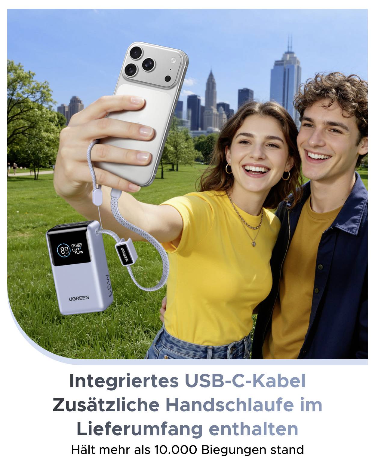 Mladý pár si pořizuje selfie v parku s přenosnou powerbankou a integrovaným kabelem USB-C; německý text říká, že je součástí extra páska na zápěstí a vydrží přes 10 000 ohnutí.