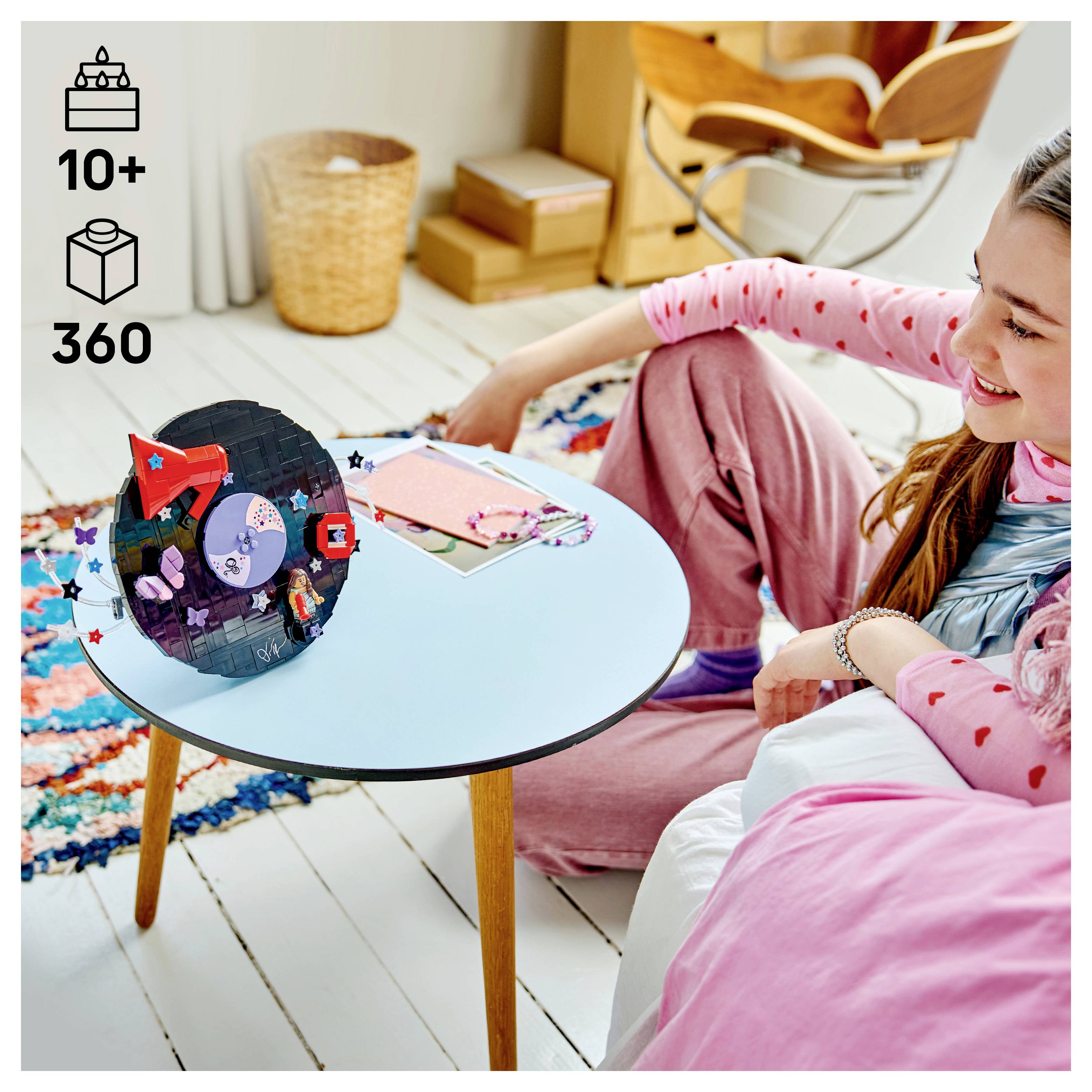 Dívka sedí na podlaze vedle kulatého stolu s barevným modelem z řemeslné sady; ikony ukazují "10+" a "360" kusů, což naznačuje stavebnici.