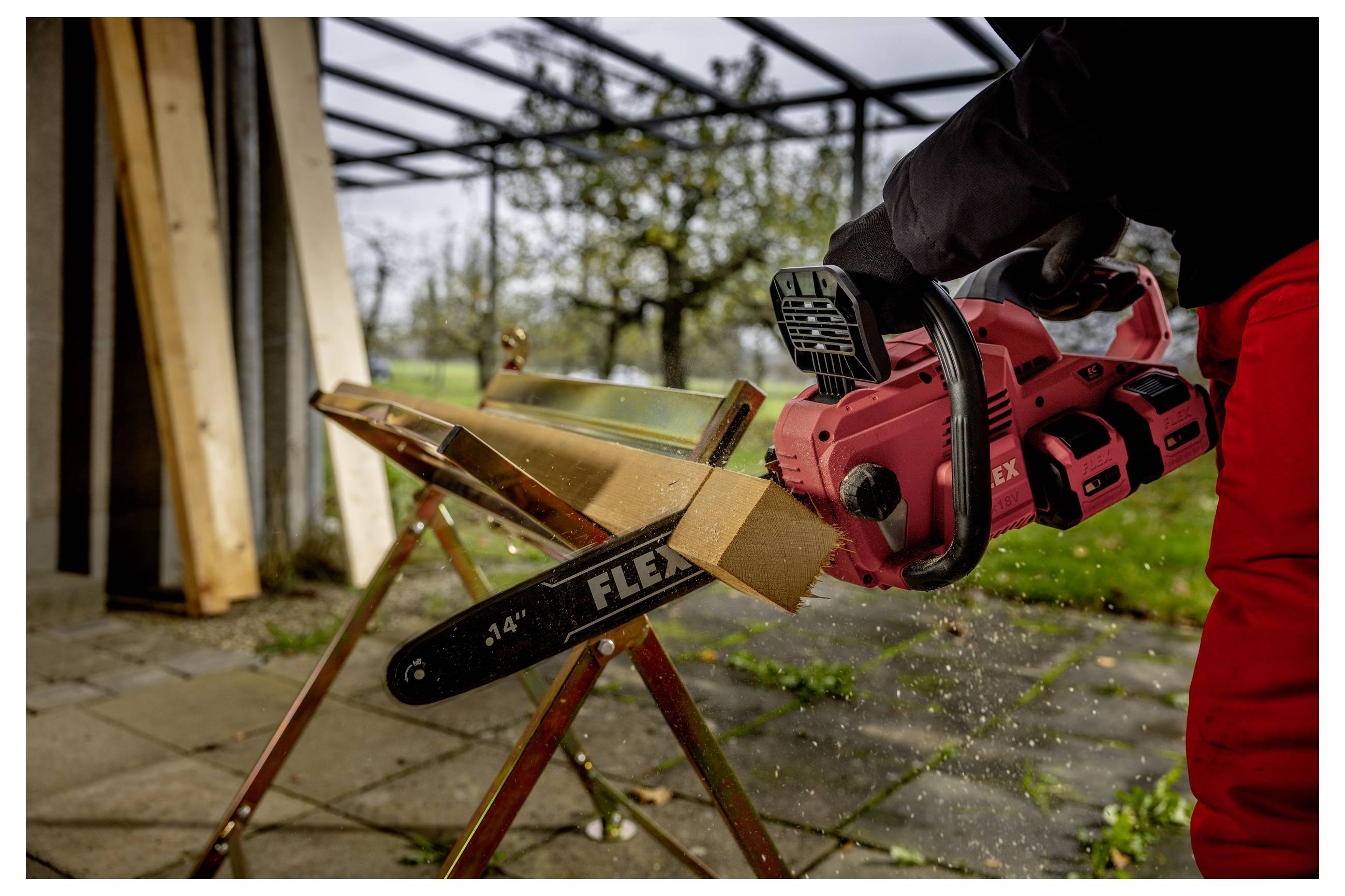 Osoba používající červenou motorovou pilu k řezání desky upevněné v truhlářské svěrce na pile na třísnění v outdoor pracovní ploše.
