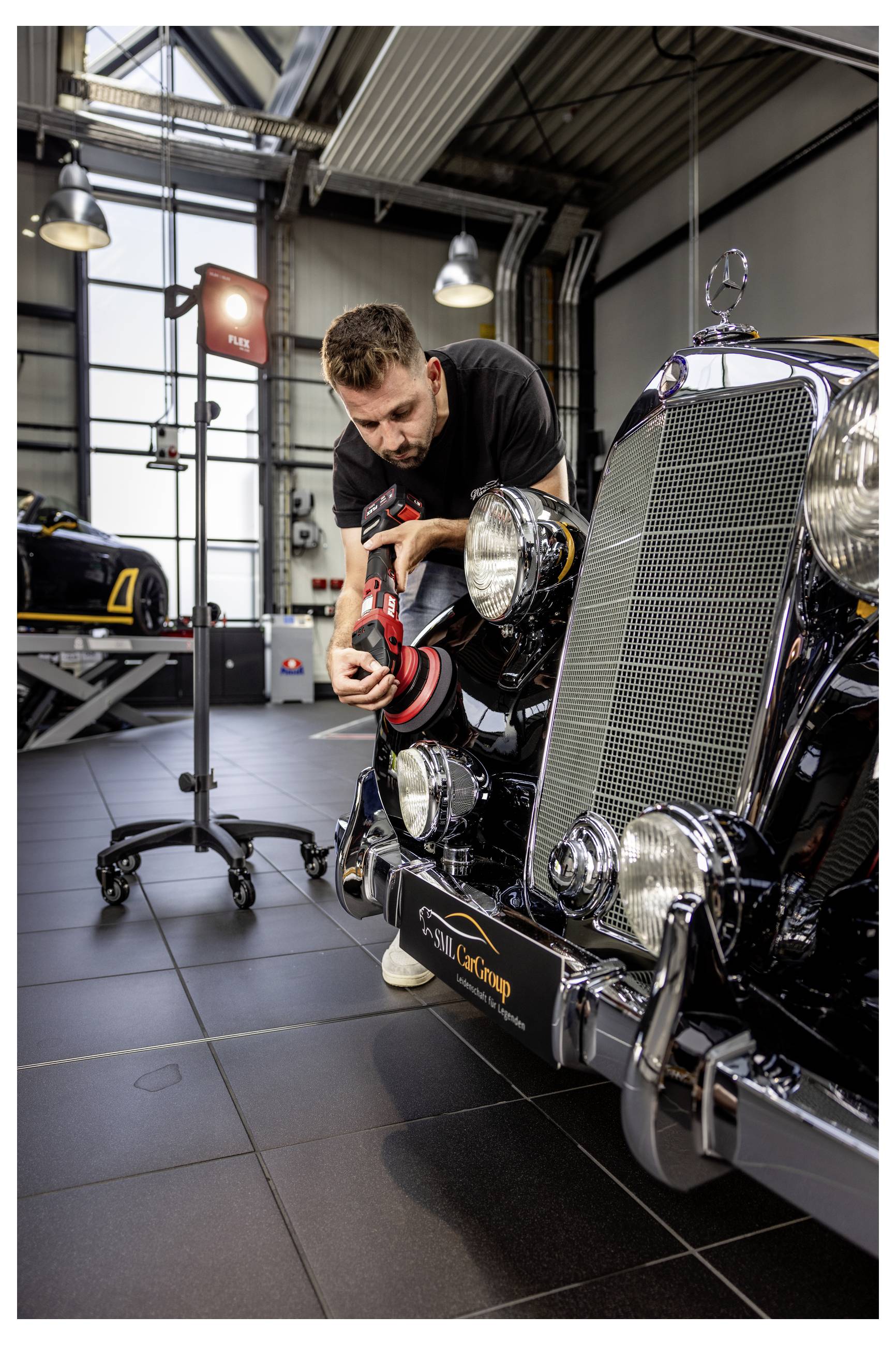 Mechanik leští přední masku a reflector vintage automobilu v dílně autoservisu.