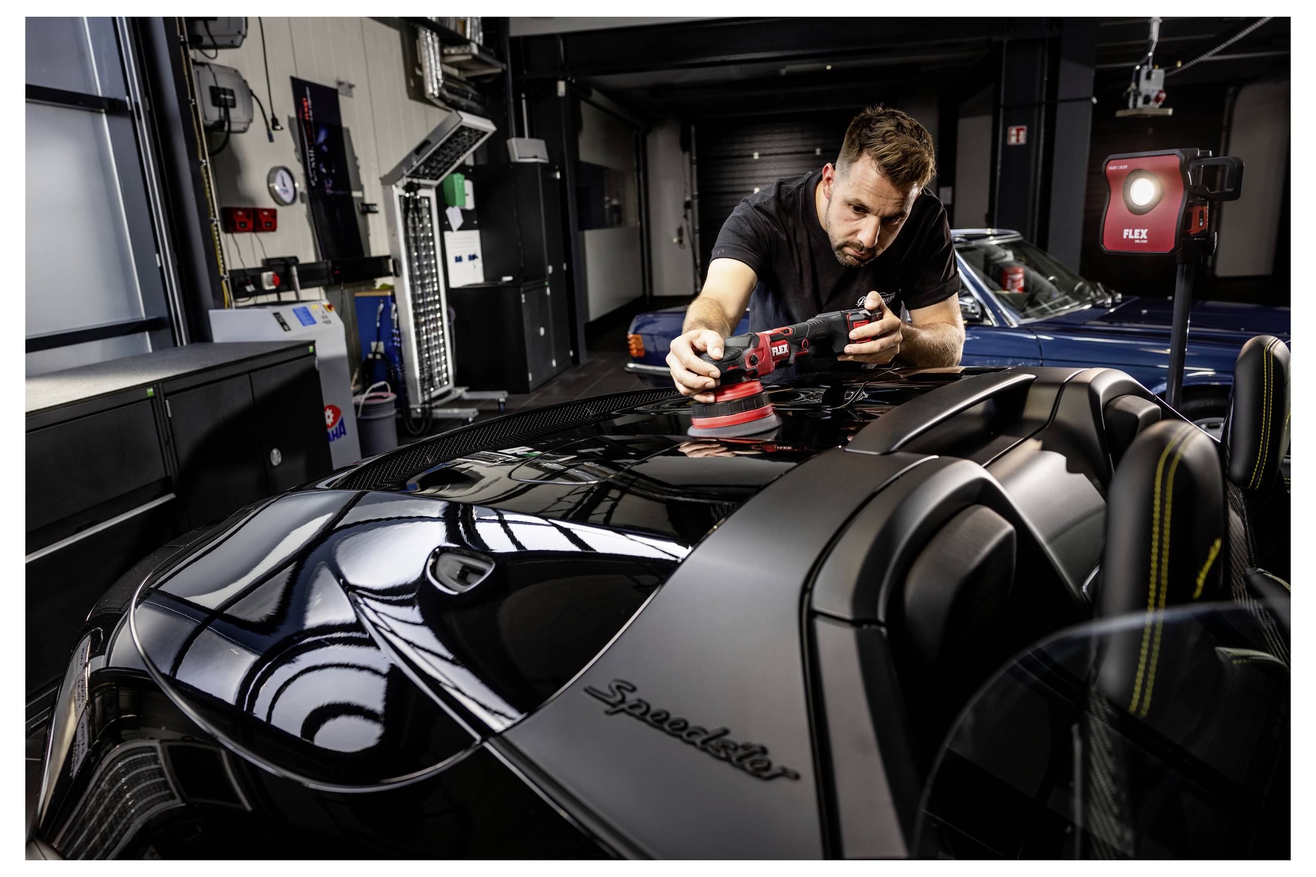 Automechanik leští lesklou černou kapotu sportovního vozu v dílně pomocí duálního rotačního leštidla.