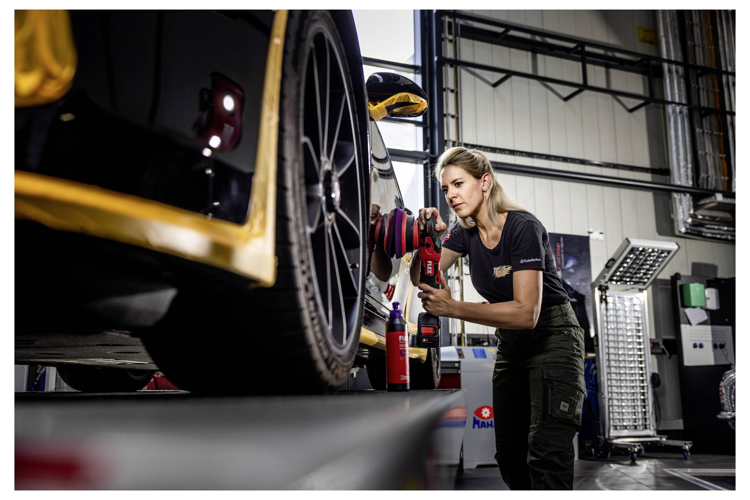 Mechanik používá elektrický nástroj k údržbě předního kola závodního vozu uvnitř automechanické dílny.