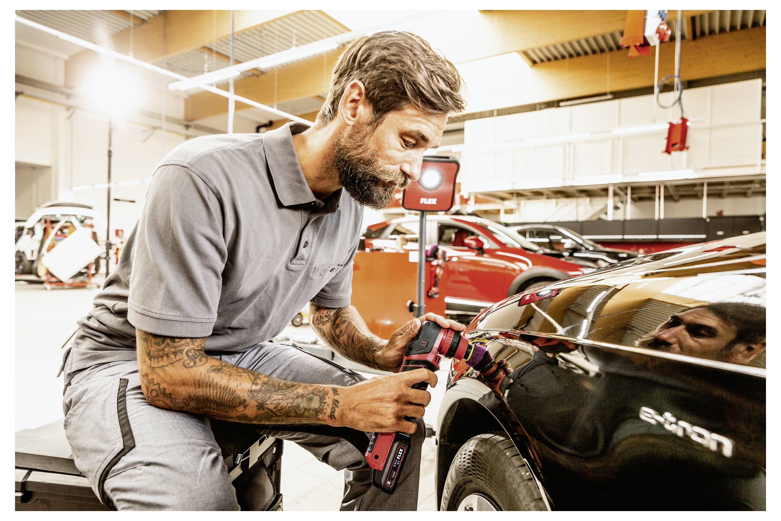 Automechanik používající bezdrátový leštěnku k vyleštění zadního panelu černého automobilu v autoopravně.