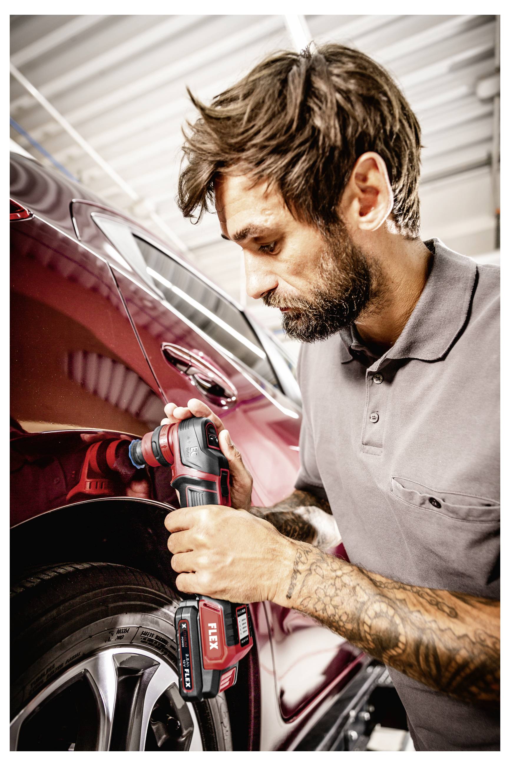 Mechanik používající bezdrátový vrtací nástroj k odstranění nebo instalaci šroubu kola automobilu na červeném vozidle v garáži.