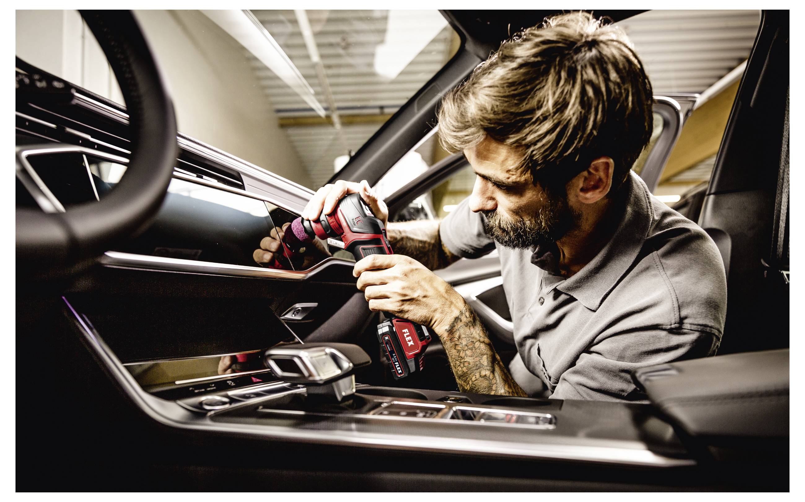 Mechanik používající bezdrátovou vrtačku k instalaci nebo opravě vnitřku dveří automobilu, zatímco se naklání do otevřeného vozidla.
