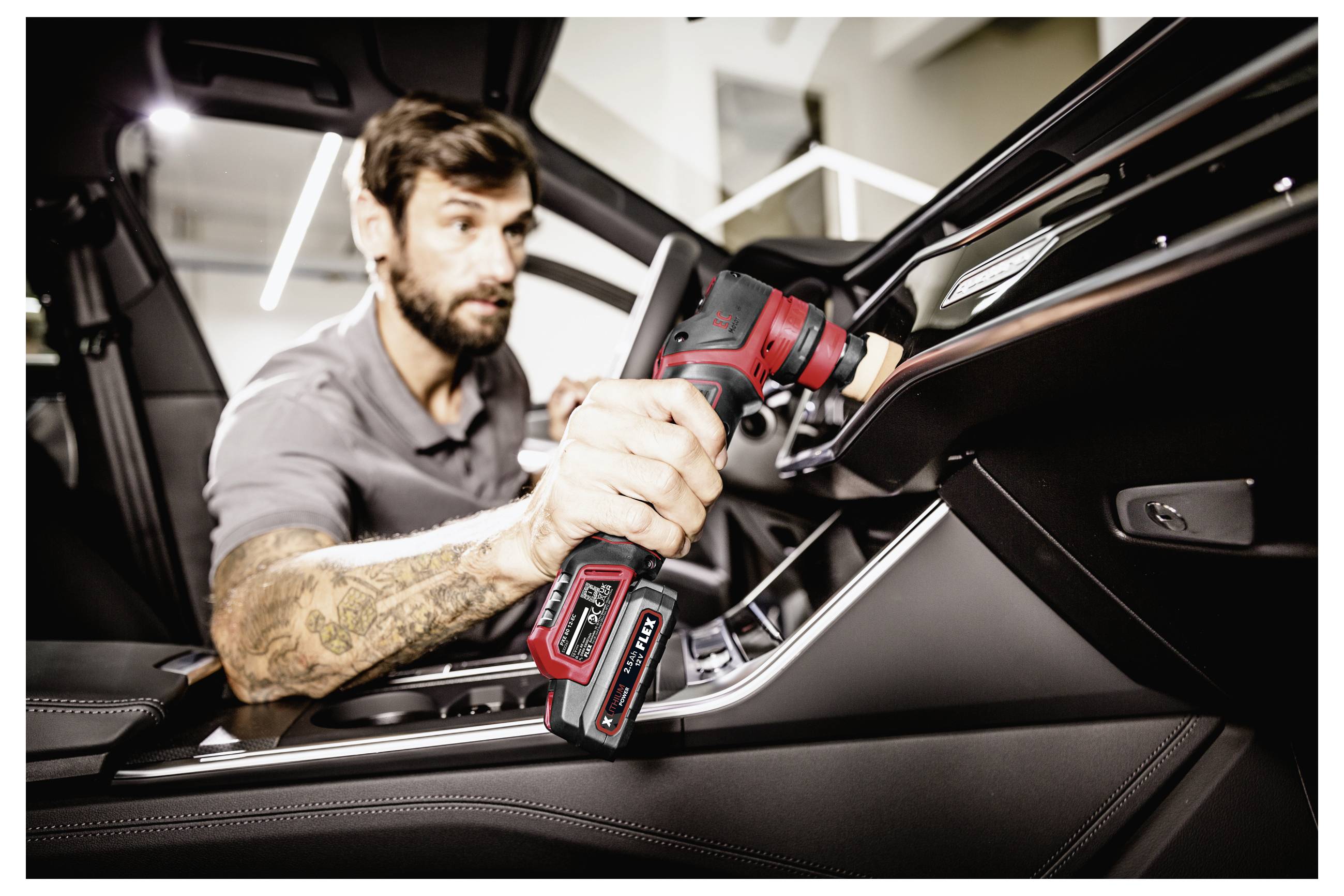 Muž leštící interiérový panel automobilu bezdrátovým elektrickým nástrojem uvnitř luxusního vozidla.