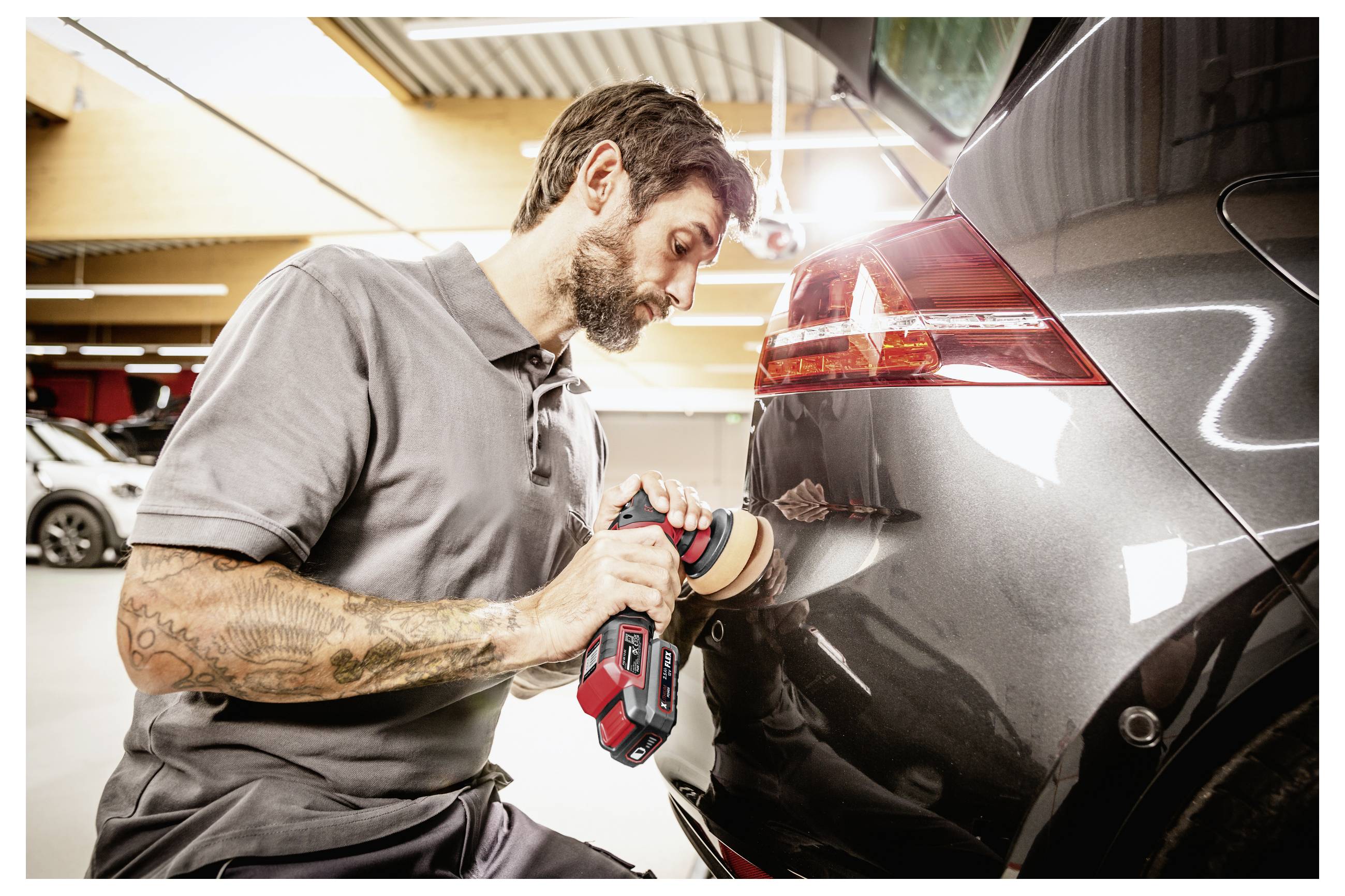 Automechanik leští zadní část černého automobilu elektrickým leštidlem v autoservisu.