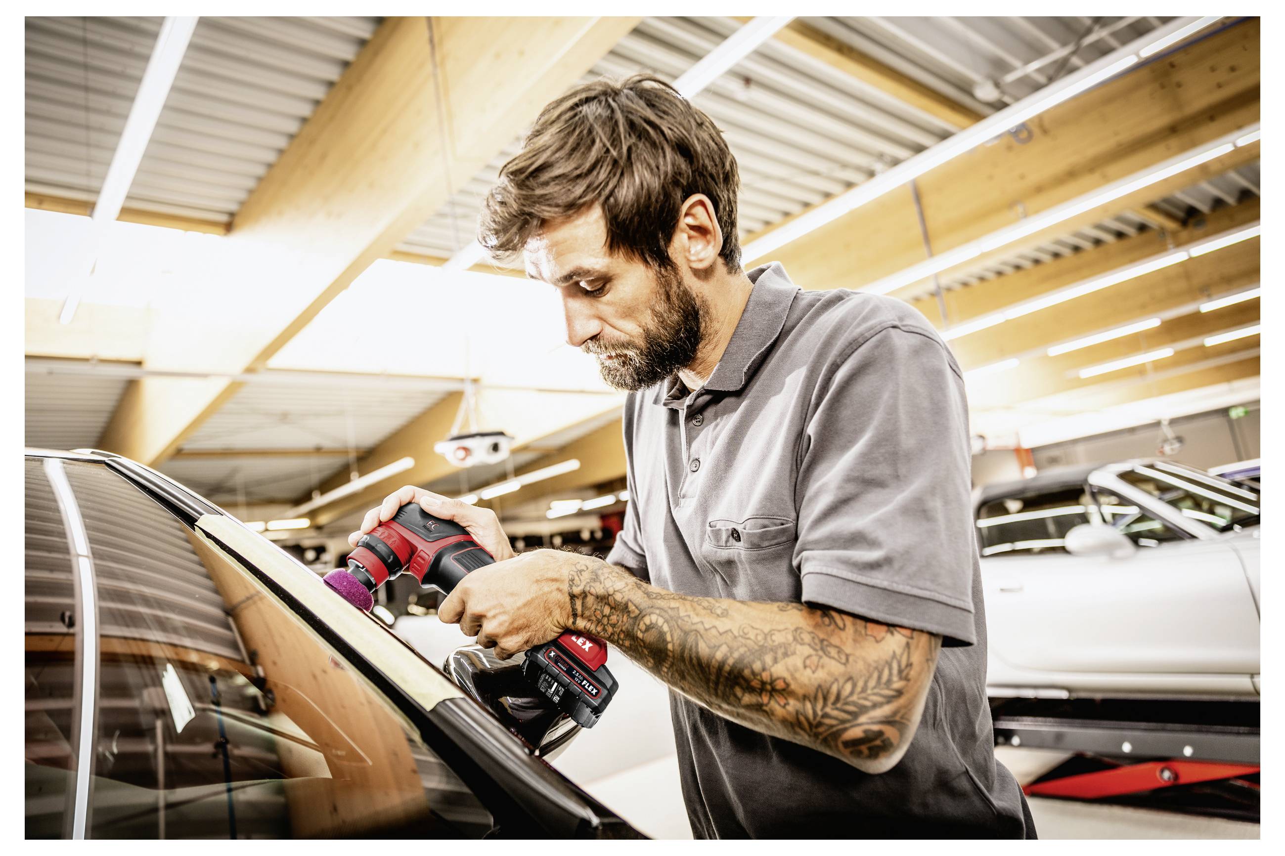 Automechanik leští okno automobilu bezdrátovým leštidlem v autodílně.