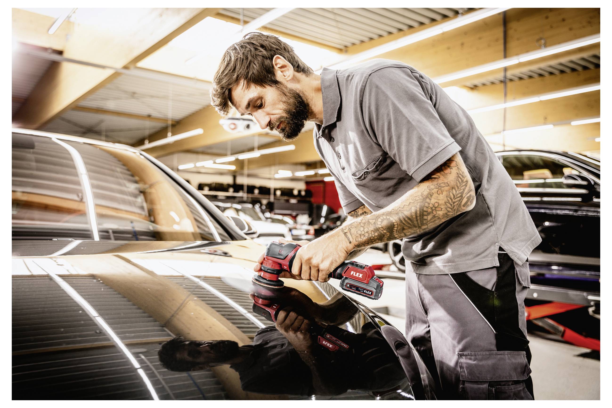 Mechanik leštící černé auto ruční elektrickým leštičem v autosalonu
