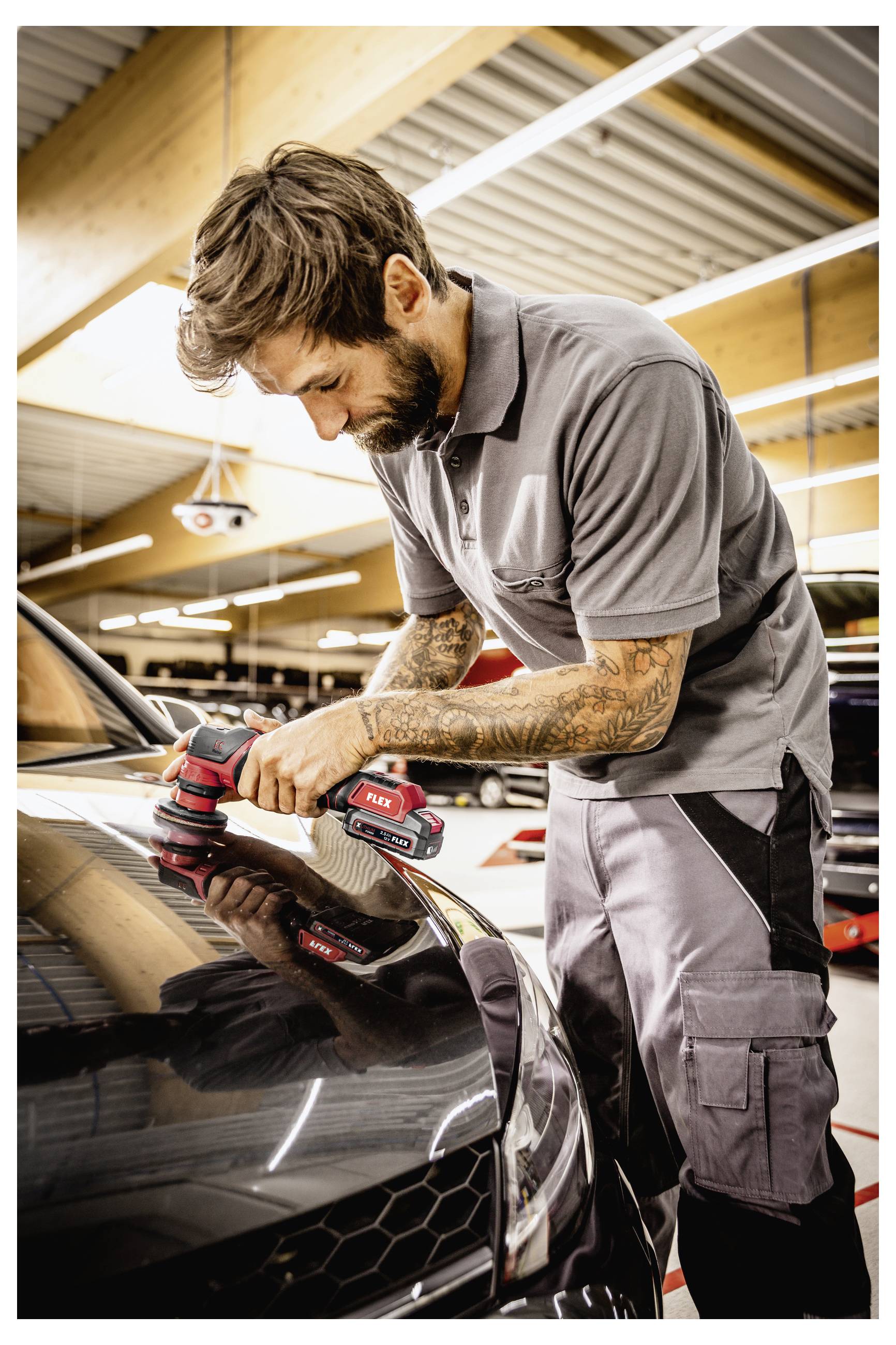 Automechanik používá elektrickou leštičku, aby vyleštil černý sportovní vůz v dílně.