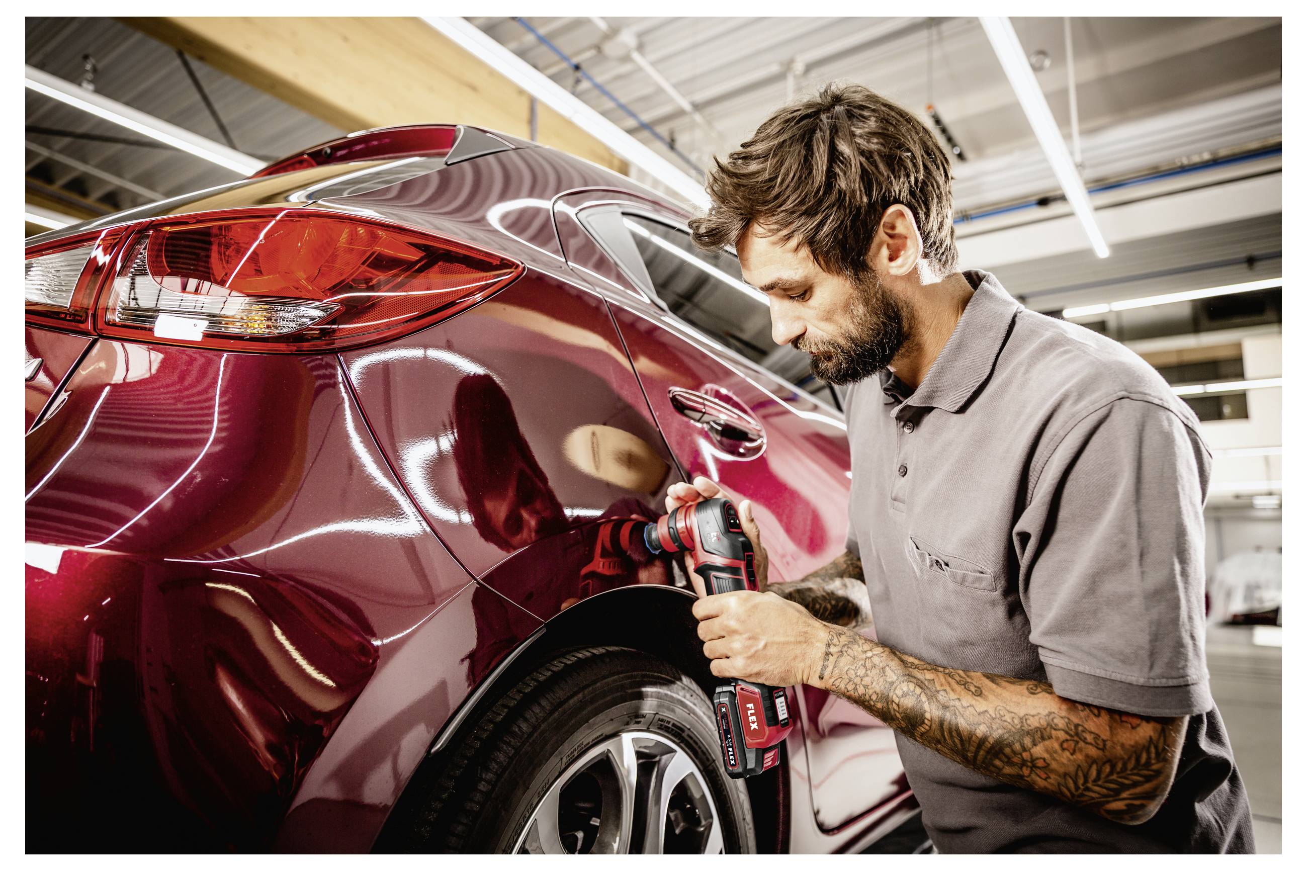 Technik leštící zadní panel bordó automobilu bezdrátovým leštičem v autodílně.
