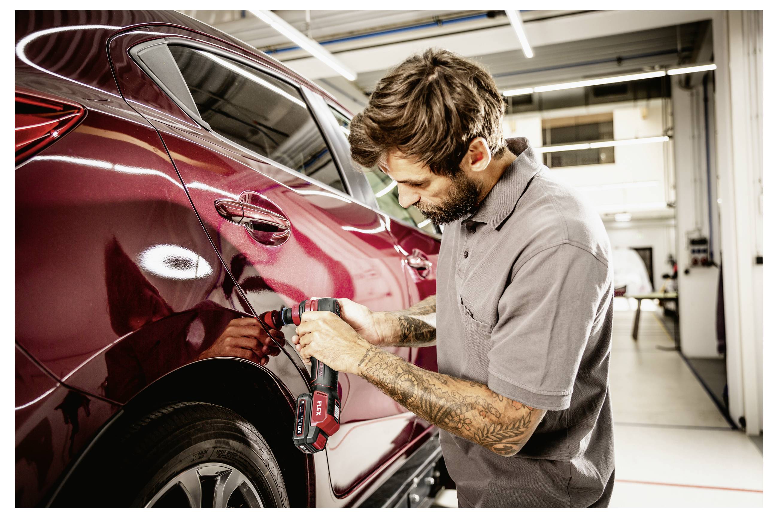 Mechanikat používající bezdrátový elektrický nástroj k odstranění promáčkliny z dveří červeného automobilu v autoservisu.