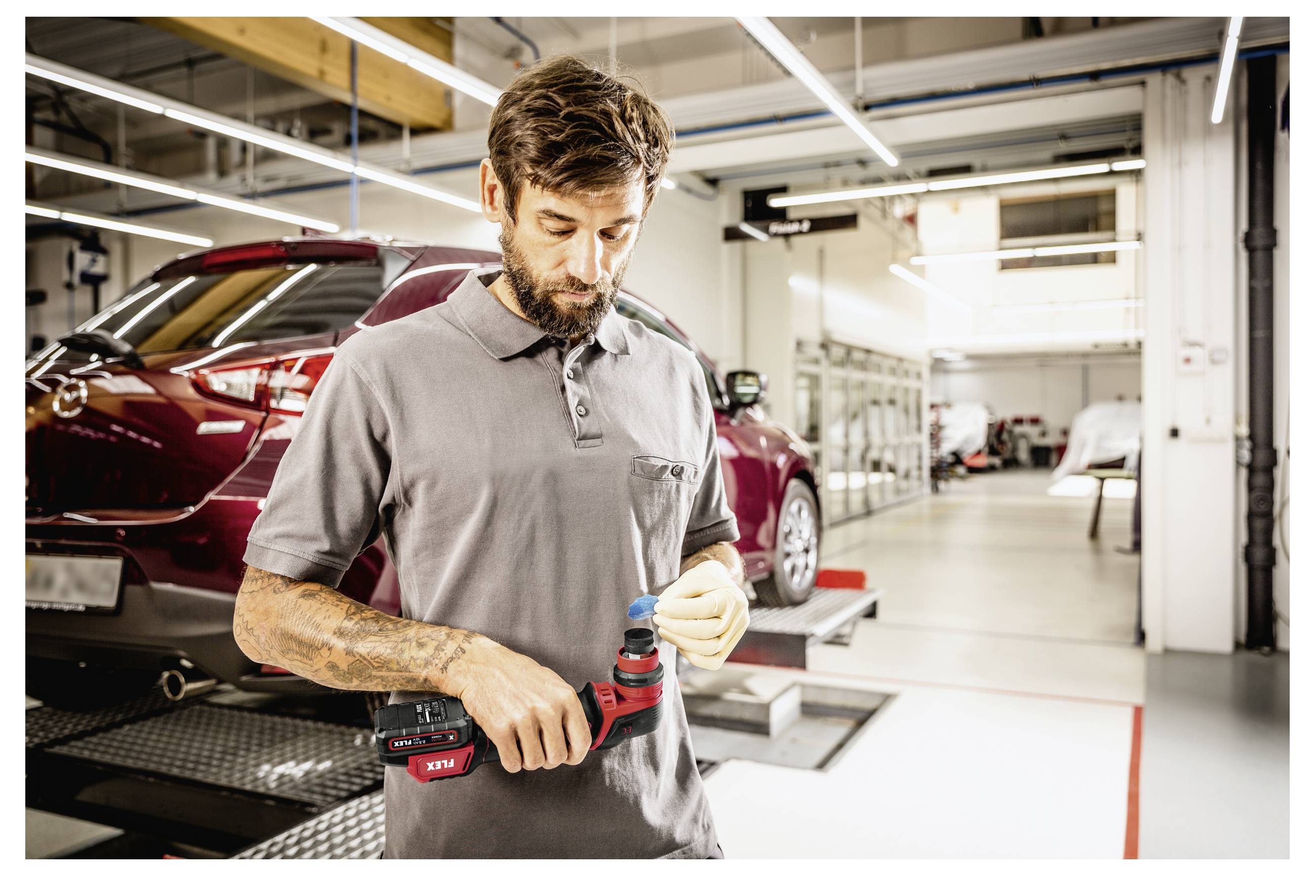 Mechanik kontroluje bezdrátový vrták v autoservisu, v pozadí je červené auto na zvedáku.