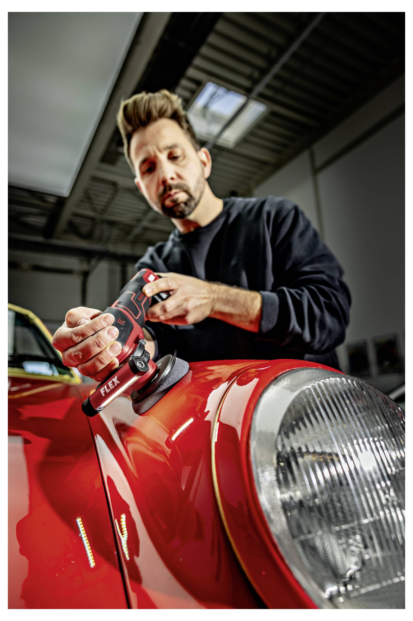 Technik používající elektrickou leštičku k vyleštění červené kapoty klasického automobilu v garáži.