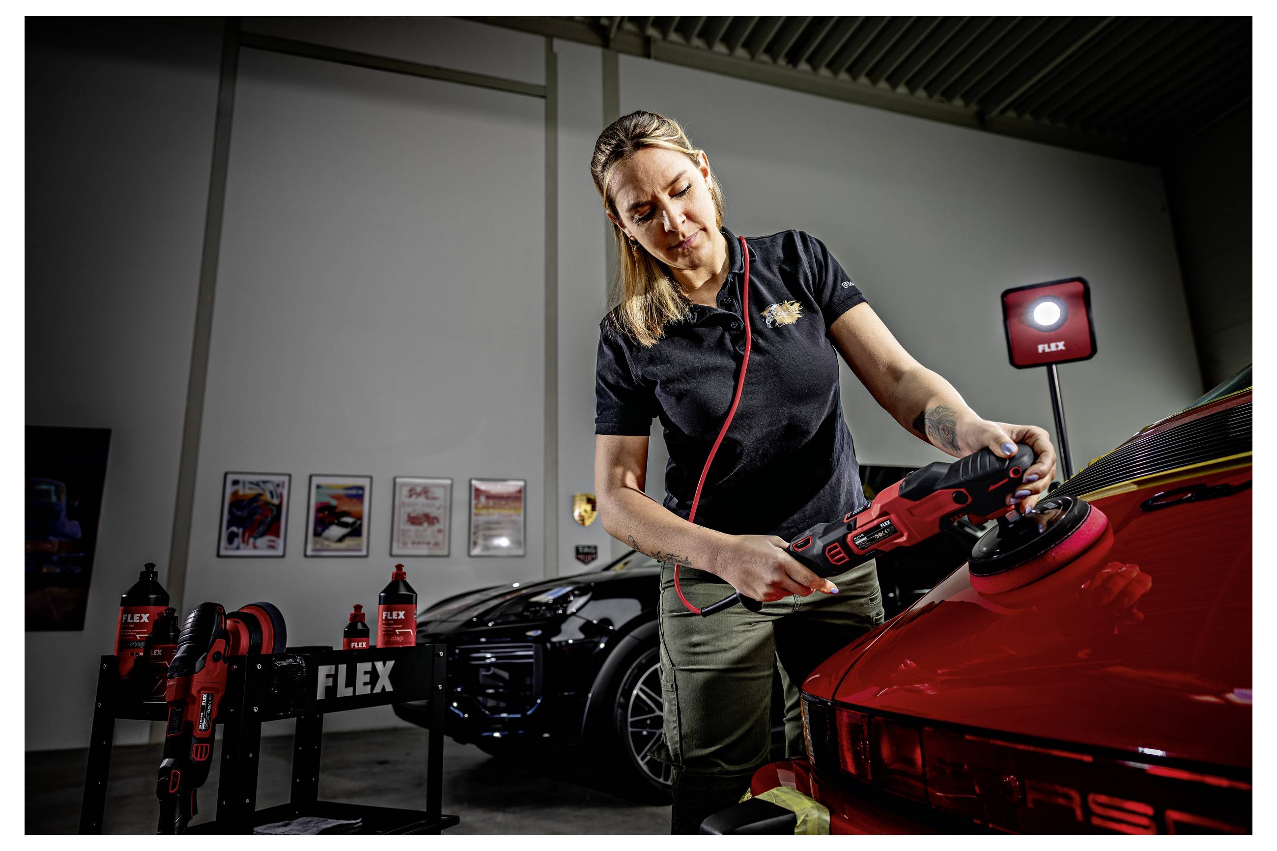 Žena používá červený FLEX elektrický leštič na červeném sportovním autě v garáži, poblíž jsou vystaveny elektrické nářadí a produkty pro péči o auto.