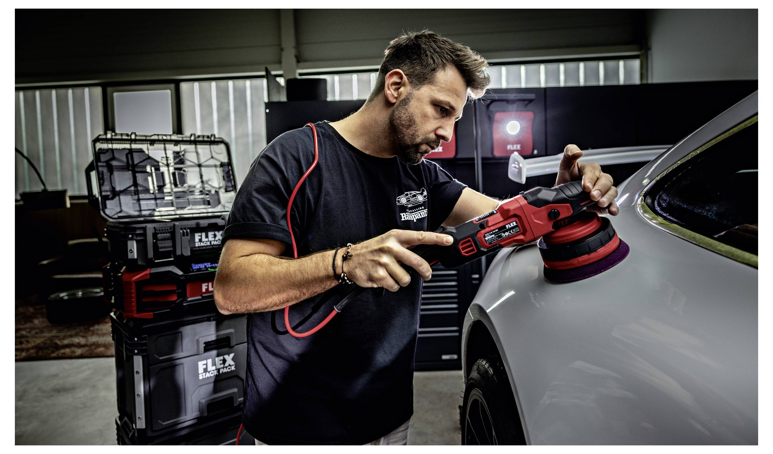 Profesionál v oblasti detailingů leští zadní čtvrtkový panel automobilu červeným pufrem v dílně, v pozadí jsou kufry s nářadím.