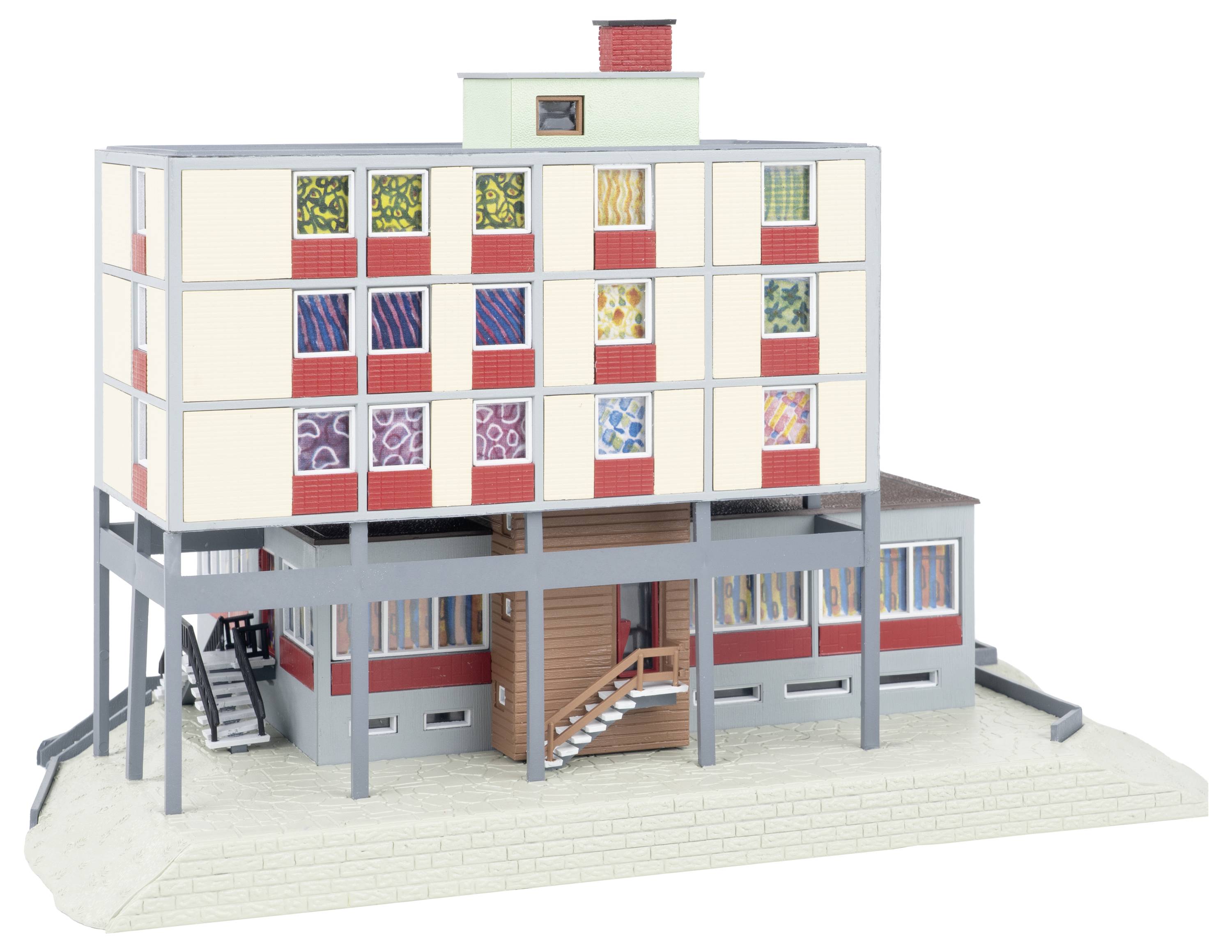 Architektonický model vícepatrové modernistické budovy na pilířích s barevnými vzorovanými okny, vnějšími schodiště a zvýšeným horním blokem přesahujícím nižší vstupní úroveň.