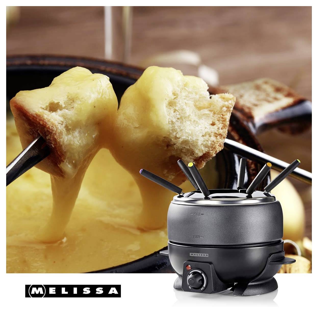 Sýrové fondue v hrnci s kostkami chleba na vidličkách, vedle černé elektrické soupravy na fondue MELISSA na dřevěném stole.