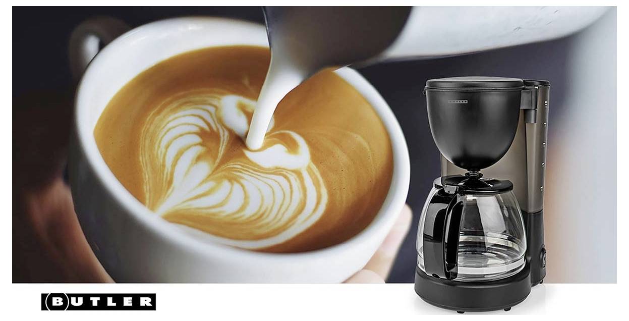 Kávovar se skleněnou konvicí vedle latte, do kterého se nalévá mléko a vytváří latte art v bílém hrnku; zobrazena značka Butler.