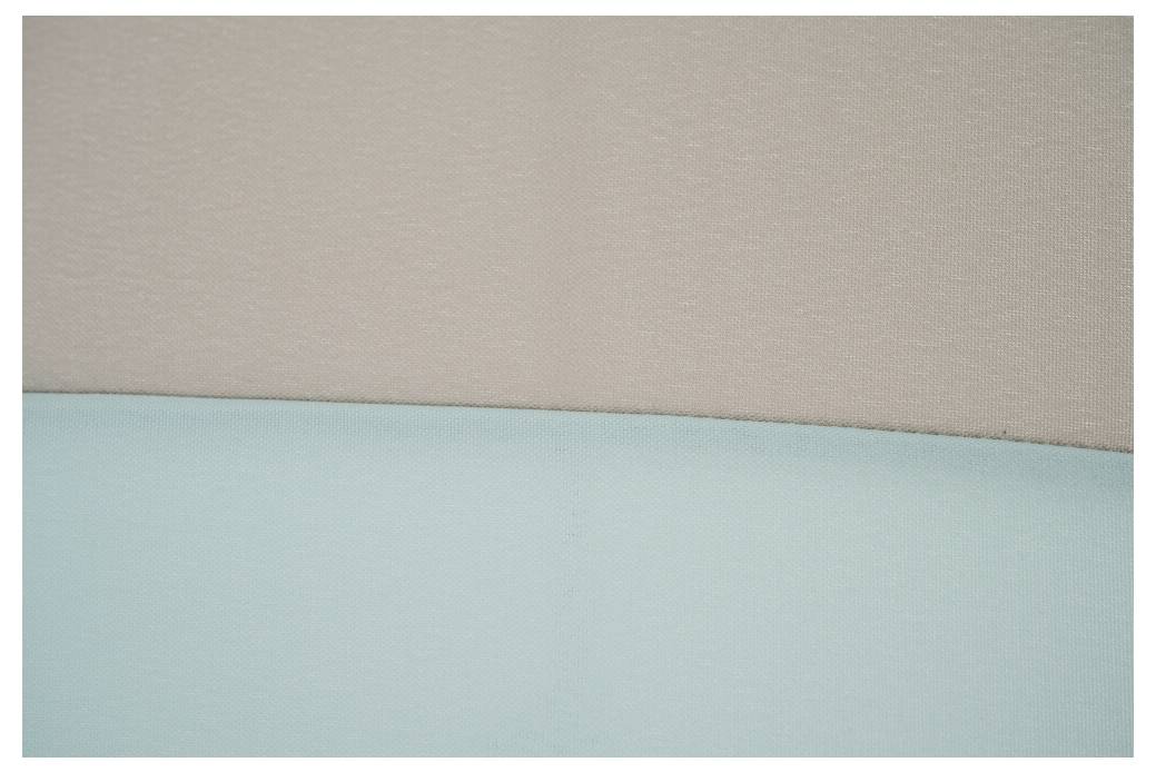 Detailní záběr béžového a světlemodrého čalounění se vodorovným švem, zobrazující pouze abstraktní struktury a barvy textilu.
