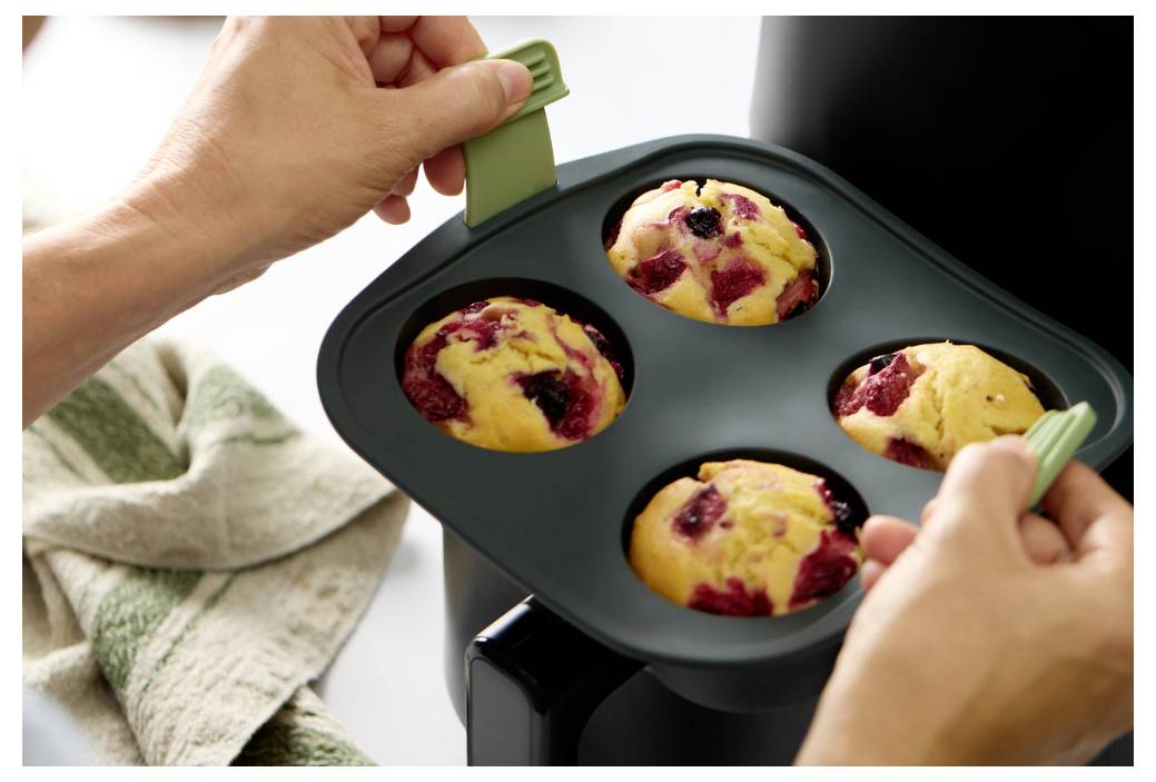 Ruce vyjímající čtyřmístný pekáč na muffiny z trouby, zobrazující čerstvě upečené borůvkové muffiny stále v plechu.