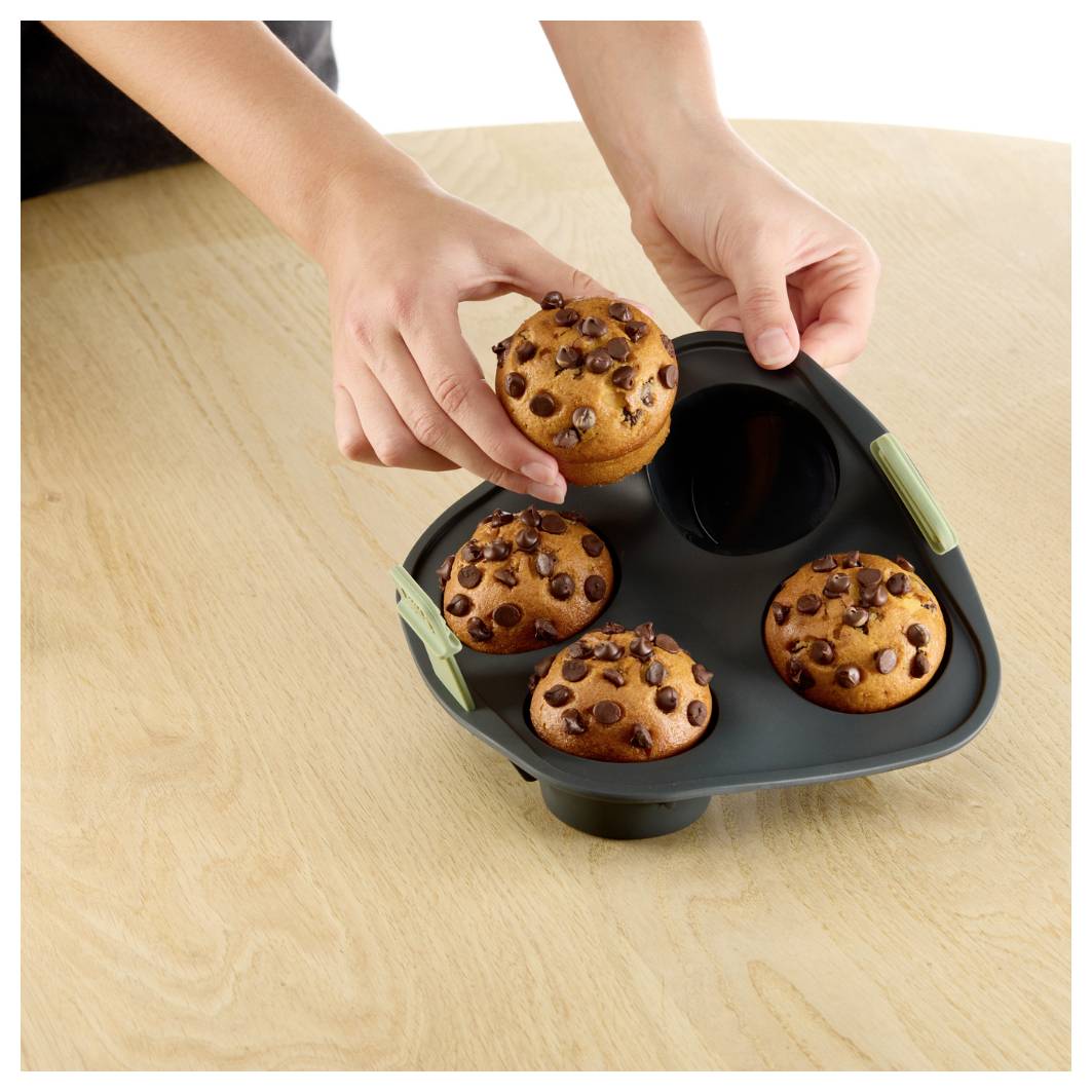 Ruce vkládající čokoládový muffin do černé čtyřdílné pekáčky na dřevěném stole.