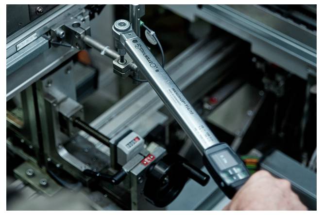 Detailní snímek technika používajícího digitální dynamometrický klíč k nastavení strojního zařízení uvnitř průmyslového montážního systému.