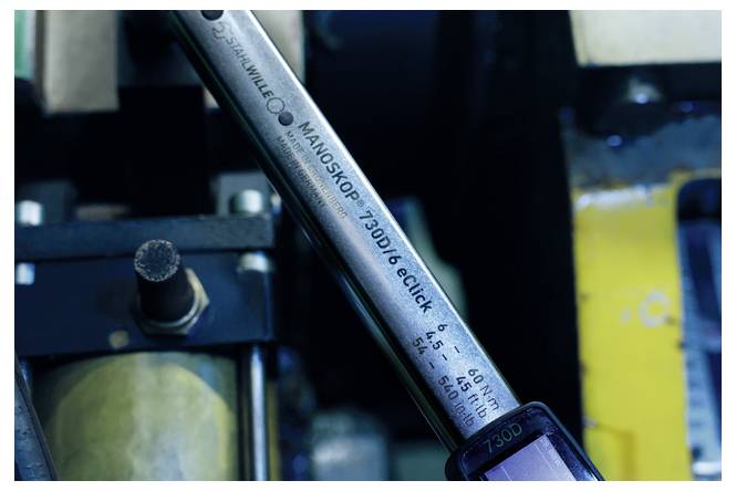 Detailní snímek kovového měřícího nástroje označeného 'MANOSKOP 730D6 eTClick' v průmyslových strojích s viditelnou stupnicí kroutícího momentu.