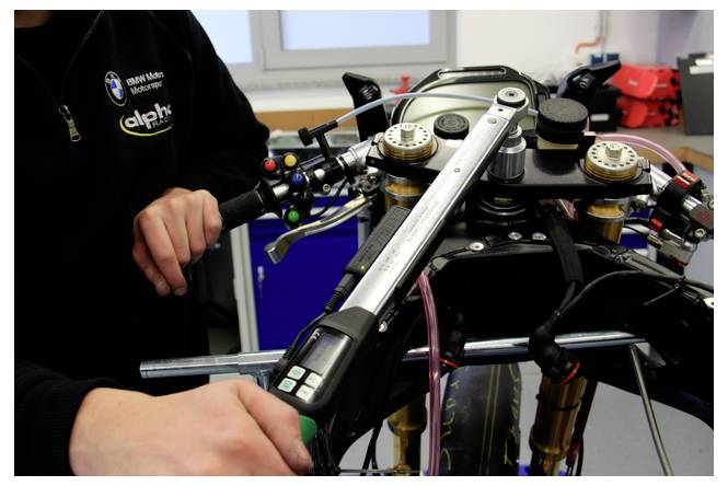 Mechanik upravuje přední část motocyklu a řidítka v dílně, s viditelným BMW značením na tričku osoby.