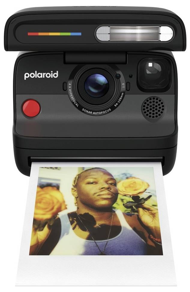 Černý instantní fotoaparát Polaroid vytiskující fotografii muže se žlutými květinami na exponovaném tisku