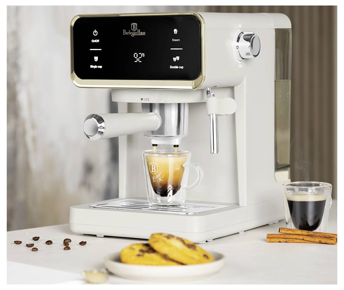 Bílý espresso stroj vaří latte do sklenice, na stole je malý černý espresso šálek, skořicové tyčinky a pečiva.