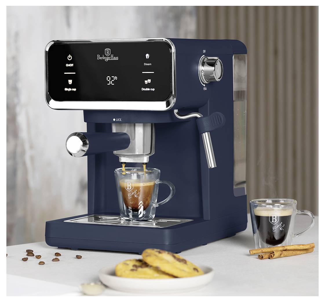Tmavá espresso mlýn připravující kávu do sklenice, s malým latté vedle ní, zrna kávy, sušenky a skořice na stole.