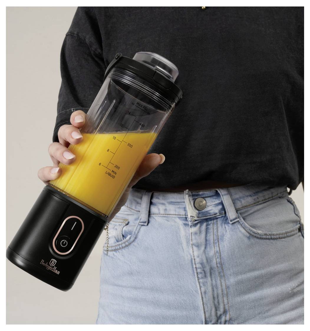 Osoba držící přenosný shaker na smoothie naplněný oranžovým smoothie na jednoduchém pozadí.
