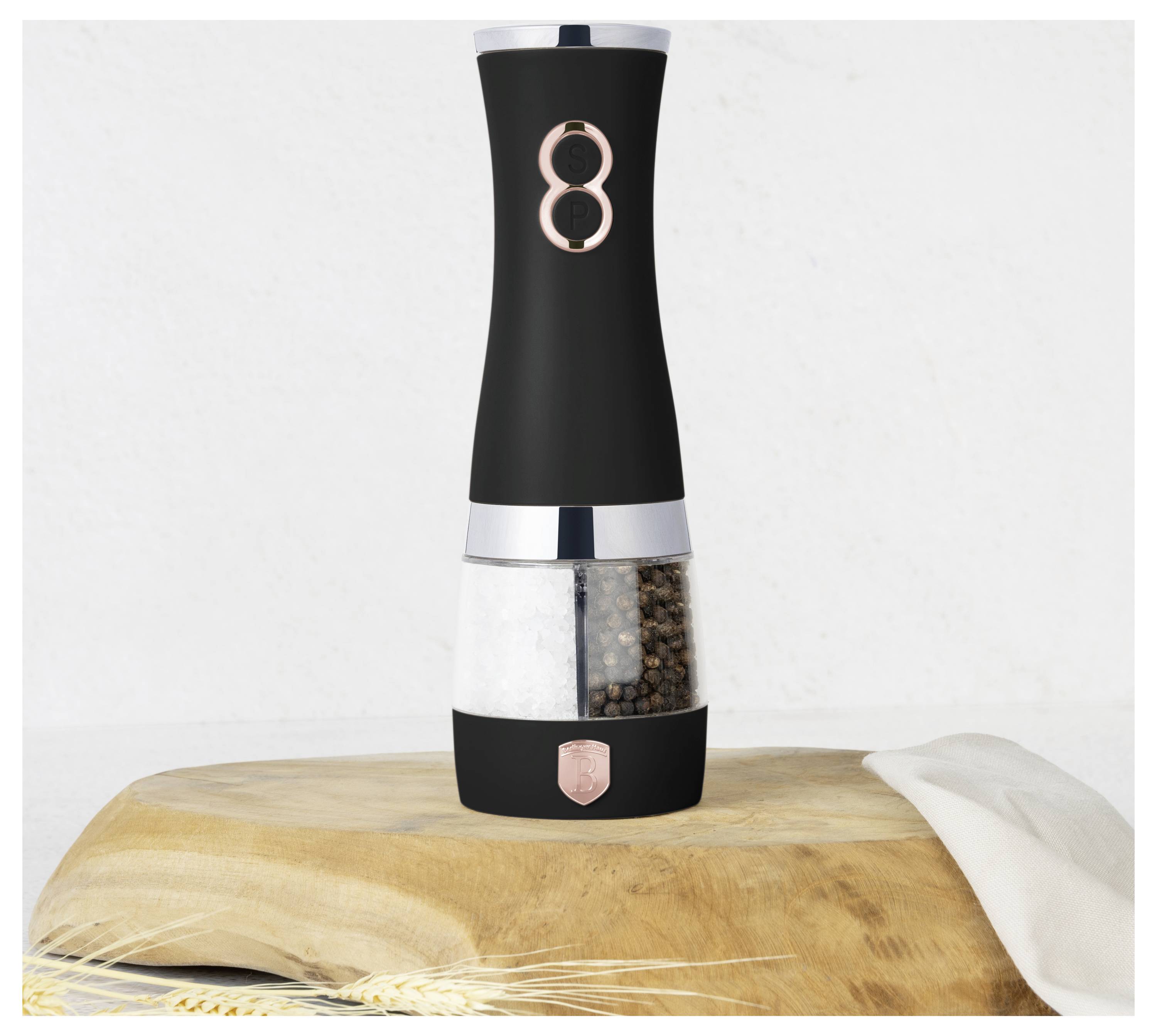 Moderní elektrický mlýnek na sůl a pepř v černé barvě s rose-gold prvky stojící na dřevěné desce.