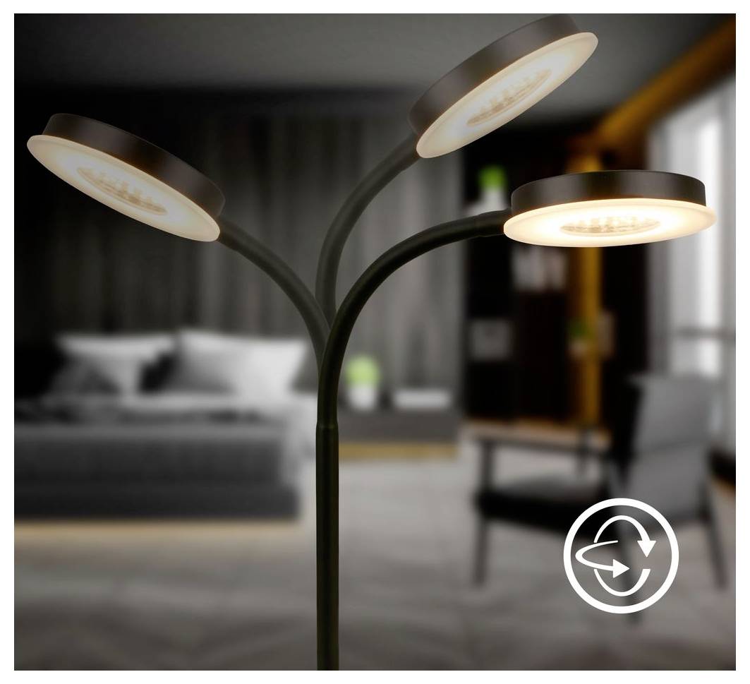 Třívlákitá moderní podlahová lampa září teplým světlem v rozmazaném pokoji, s bílou kruhovou ikonou šipky v pravém dolním rohu.