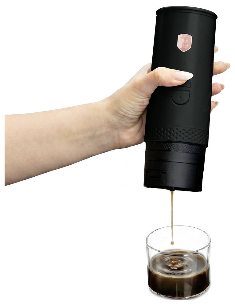 Ruka držící přenosný černý kávovář, který nalévá espresso do číré sklenice proti bílému pozadí.