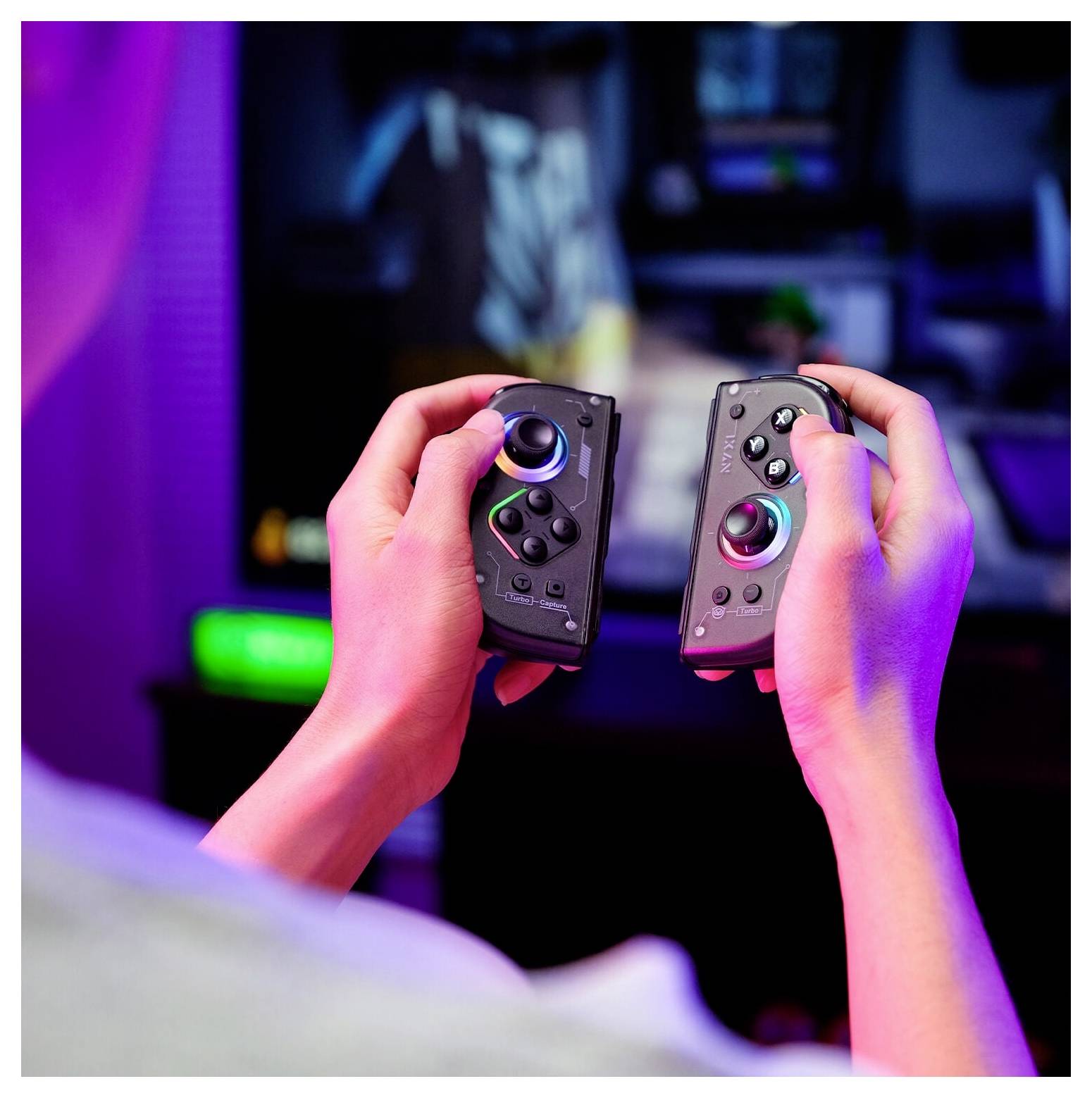 Ruce držící dva ovladače Nintendo Switch Joy-Con před rozostřeným herním setupem televize s barevným neonovým osvětlením.