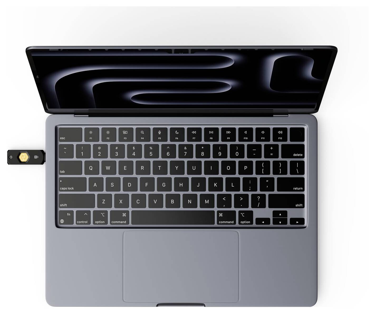 Pohled shora na laptop MacBook s otevřenou obrazovkou a bezpečnostním klíčem USB zapojeným na levé straně.