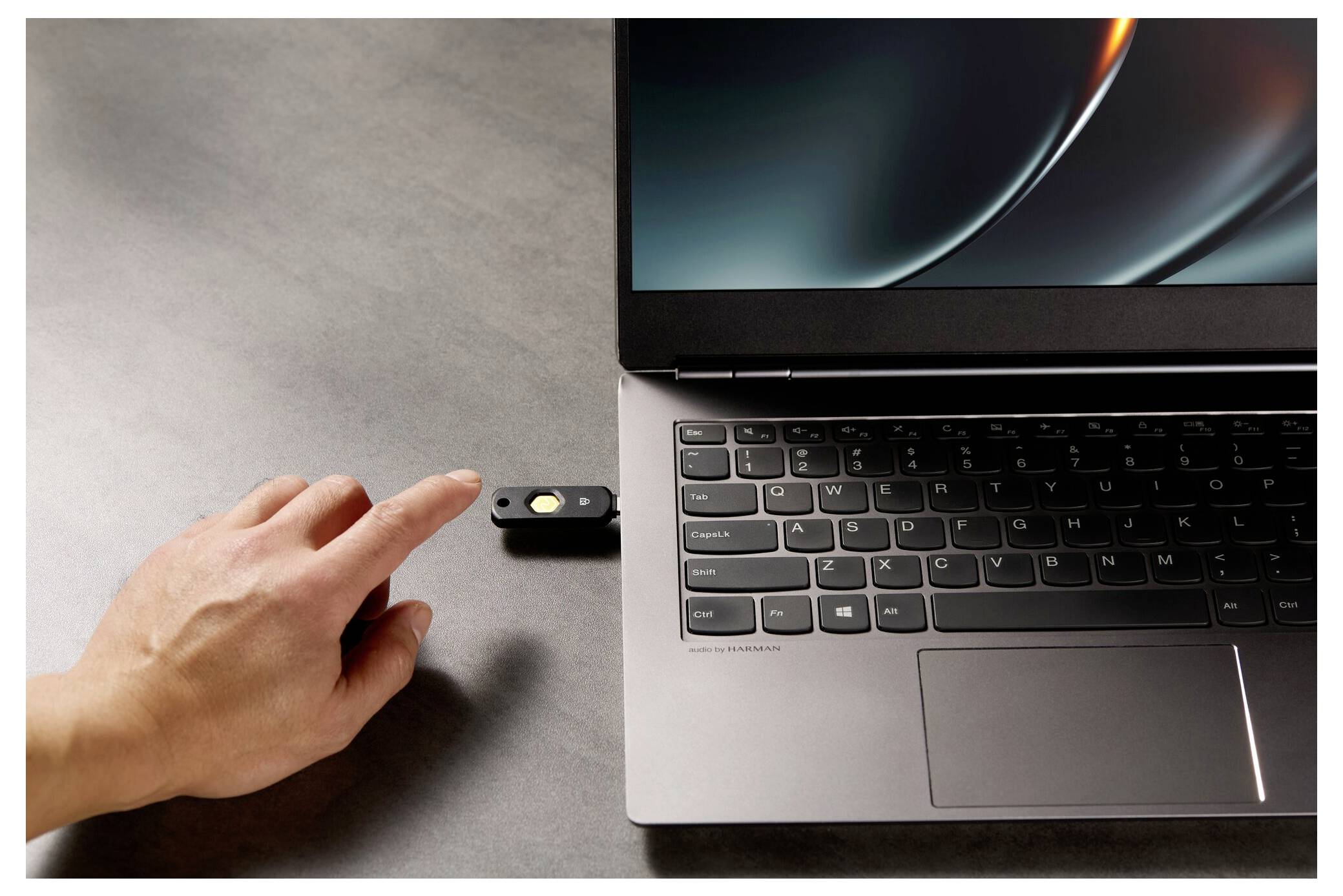Ruka připojuje USB flash disk k notebooku vedle klávesnice a touchpadu na šedém stole.