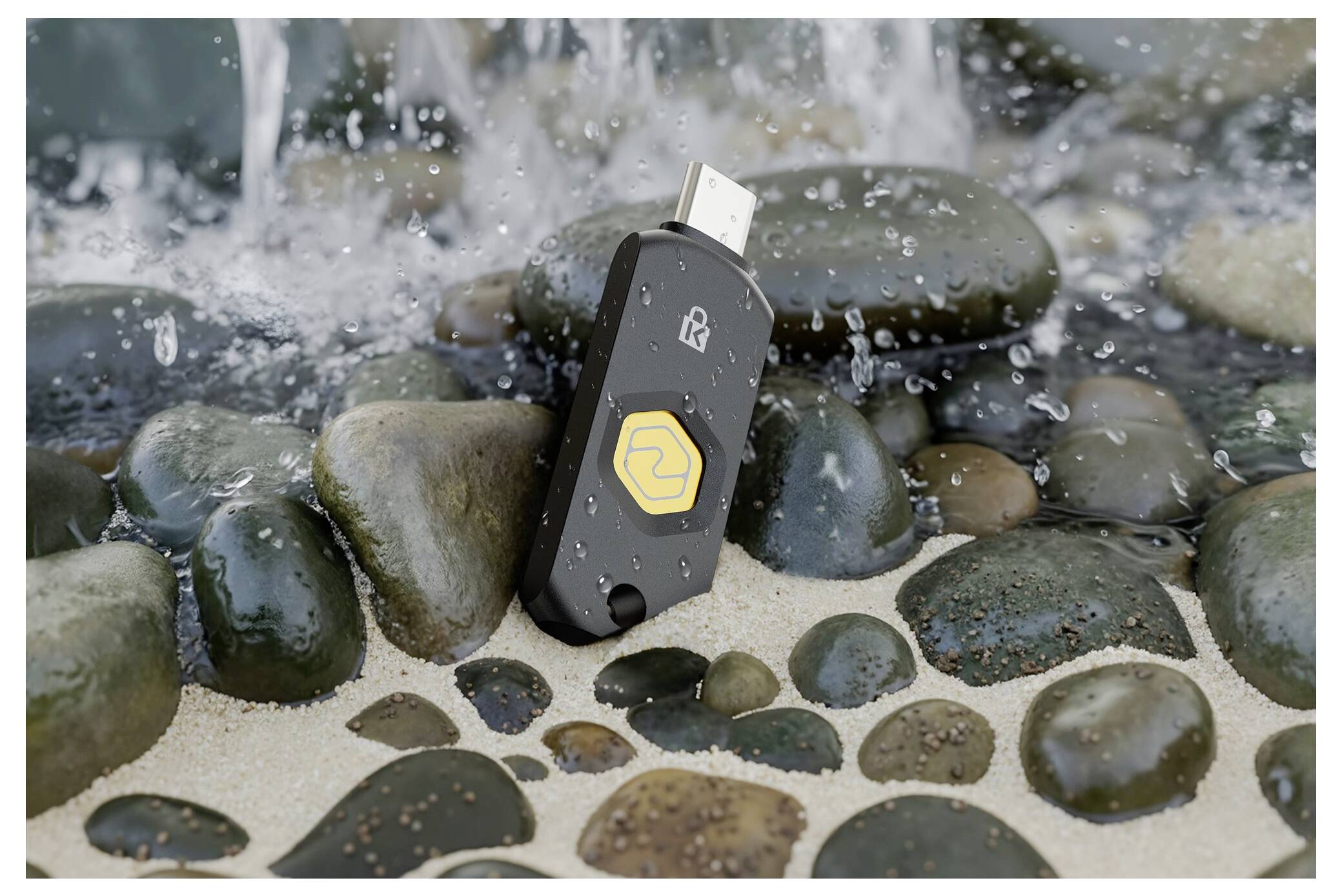 Voděodolný USB flash disk se žlutým logem stojí mezi mokrými kameny, zatímco kolem něj stříká voda.
