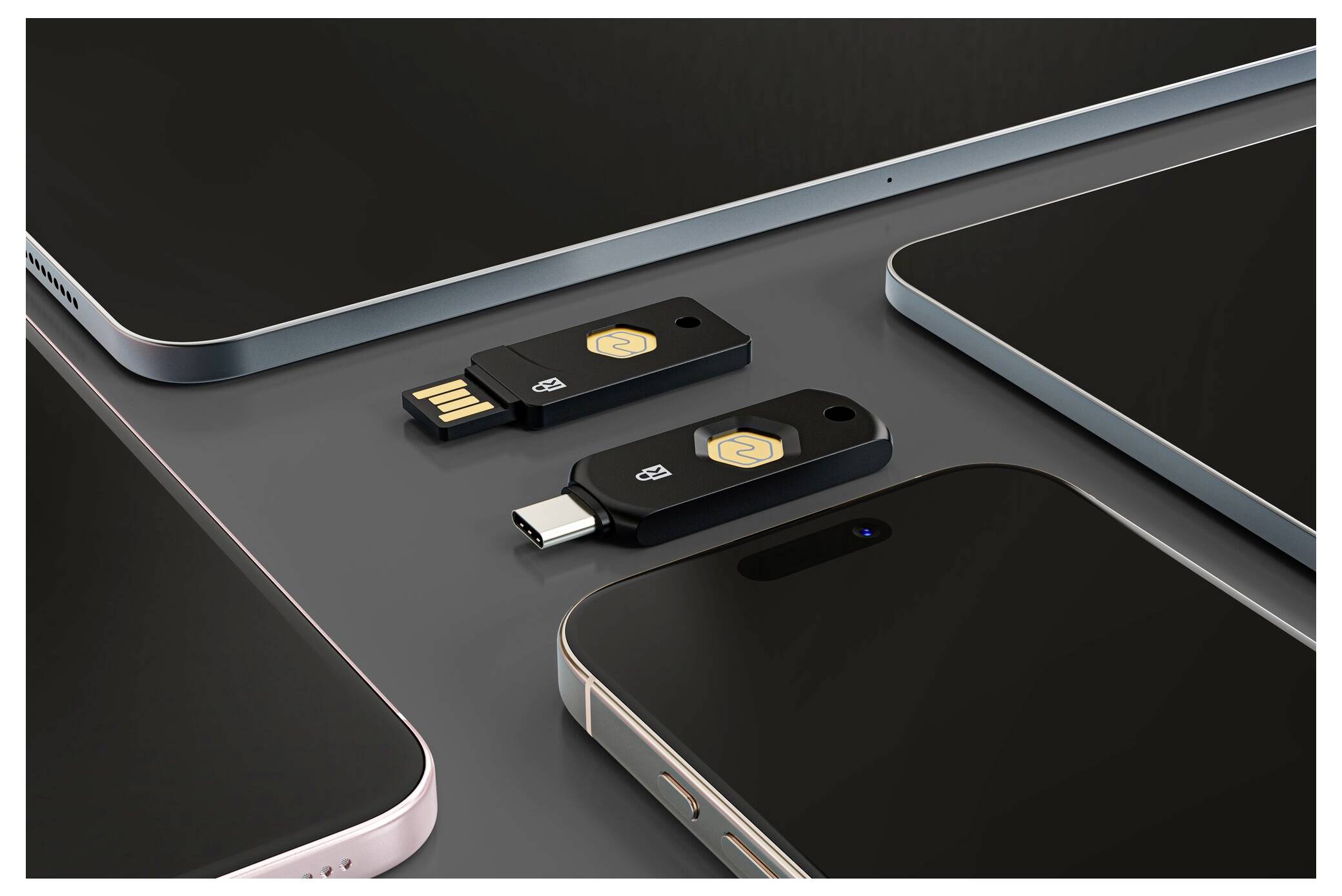 Dva USB flash disky, jeden USB-A a jeden USB-C, uspořádané mezi několika chytrými telefony nebo tablety na tmavém povrchu.