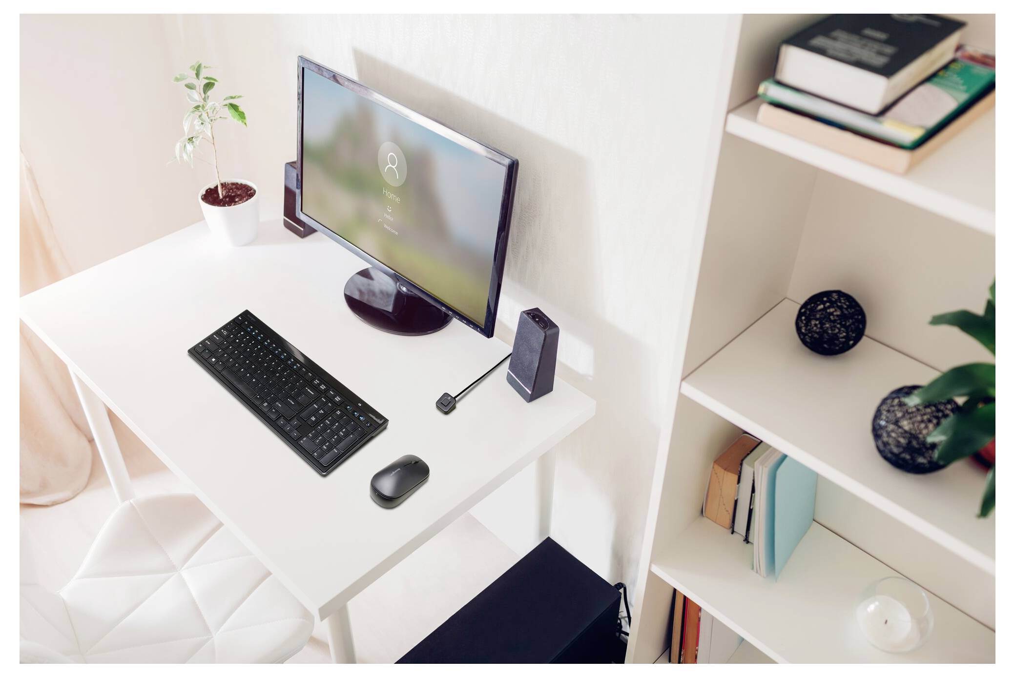 Minimalistický domácí kancelářský stůl s počítačovým monitorem, klávesnicí, myší a stolním mikrofonem vedle knihovny a malých rostlin.